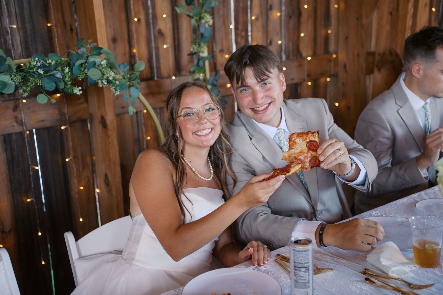 Wedding reception candid moments under string lights in a rustic barn setting.