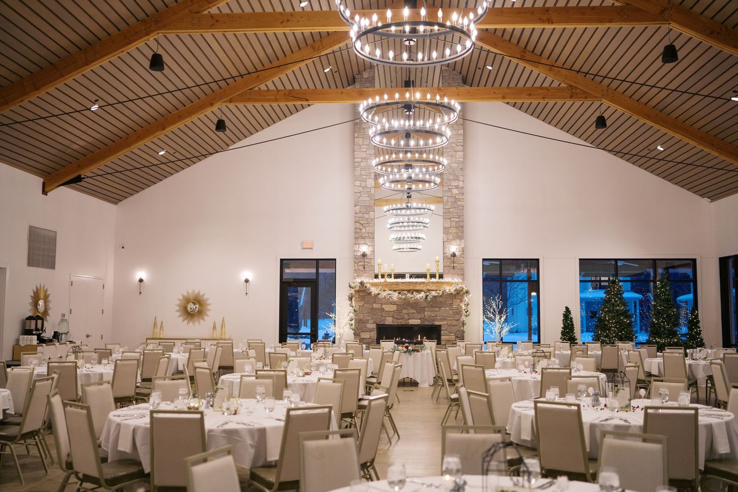 Spacious reception hall with crystal chandeliers and wooden ceiling beams set for an elegant wedding.