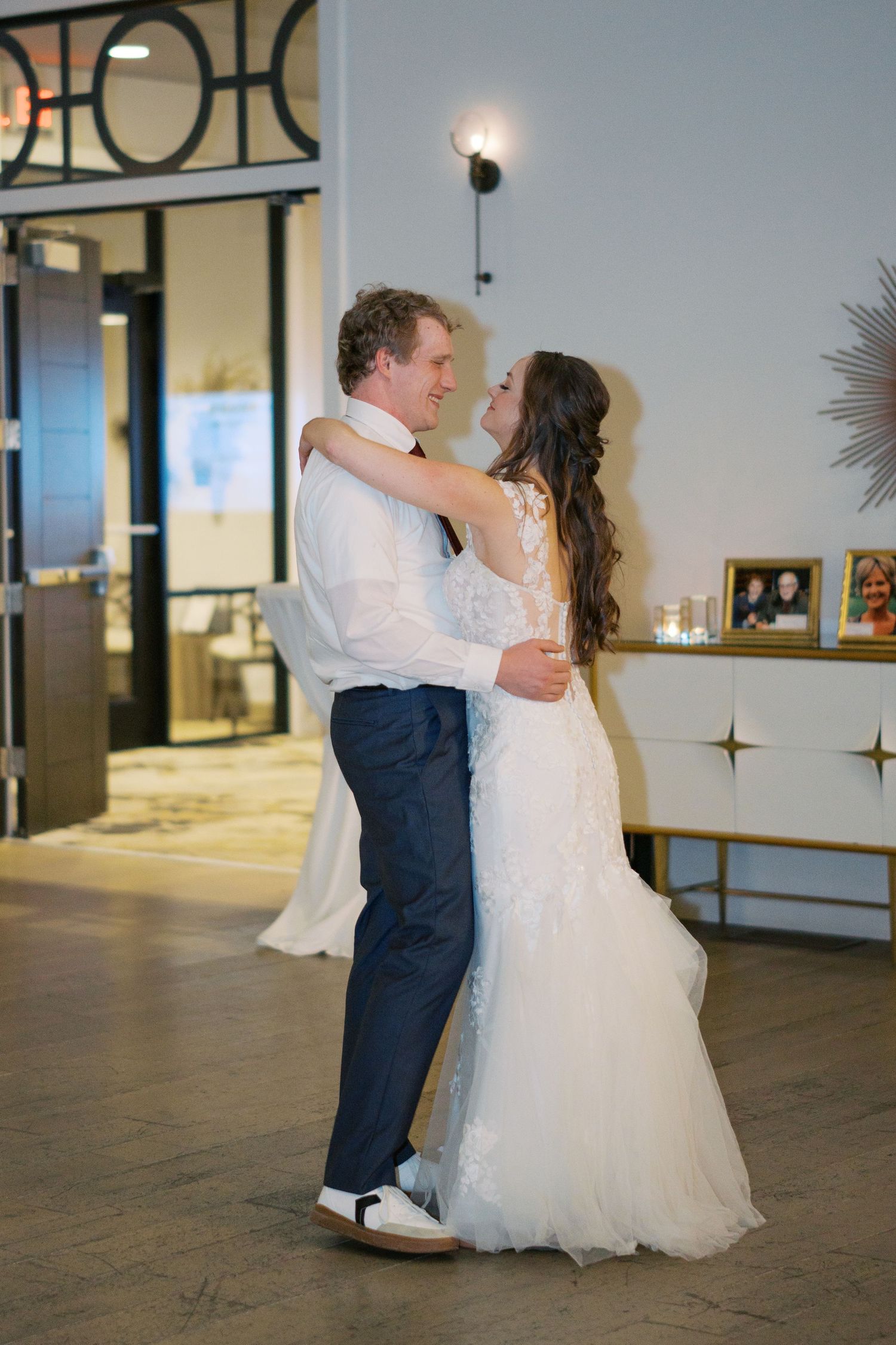 Wedding couple dancing in an elegant venue with white walls and wooden floors.