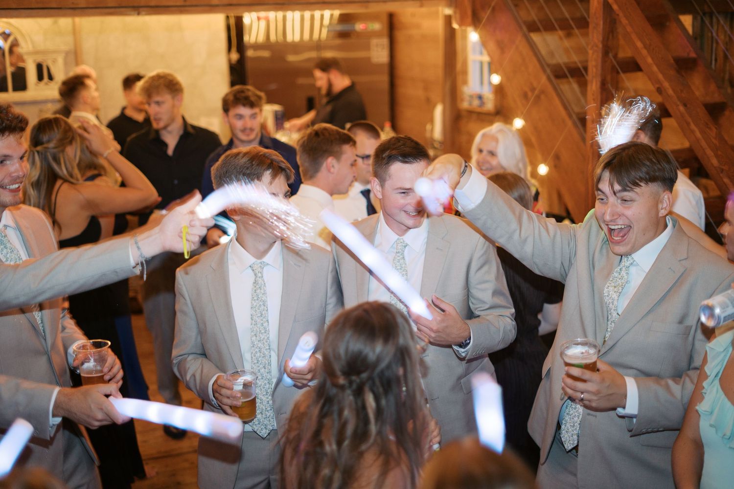 Wedding guests celebrate on the dance floor of a rustic wooden barn venue.