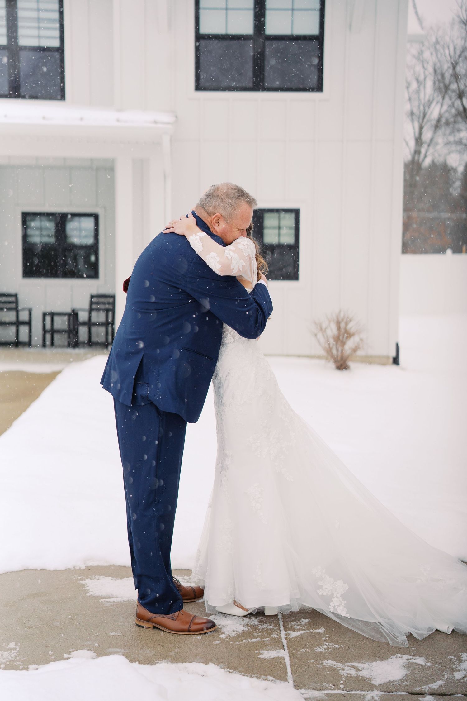 Winter wedding scene with navy suit bending down near white wedding dress in snow.