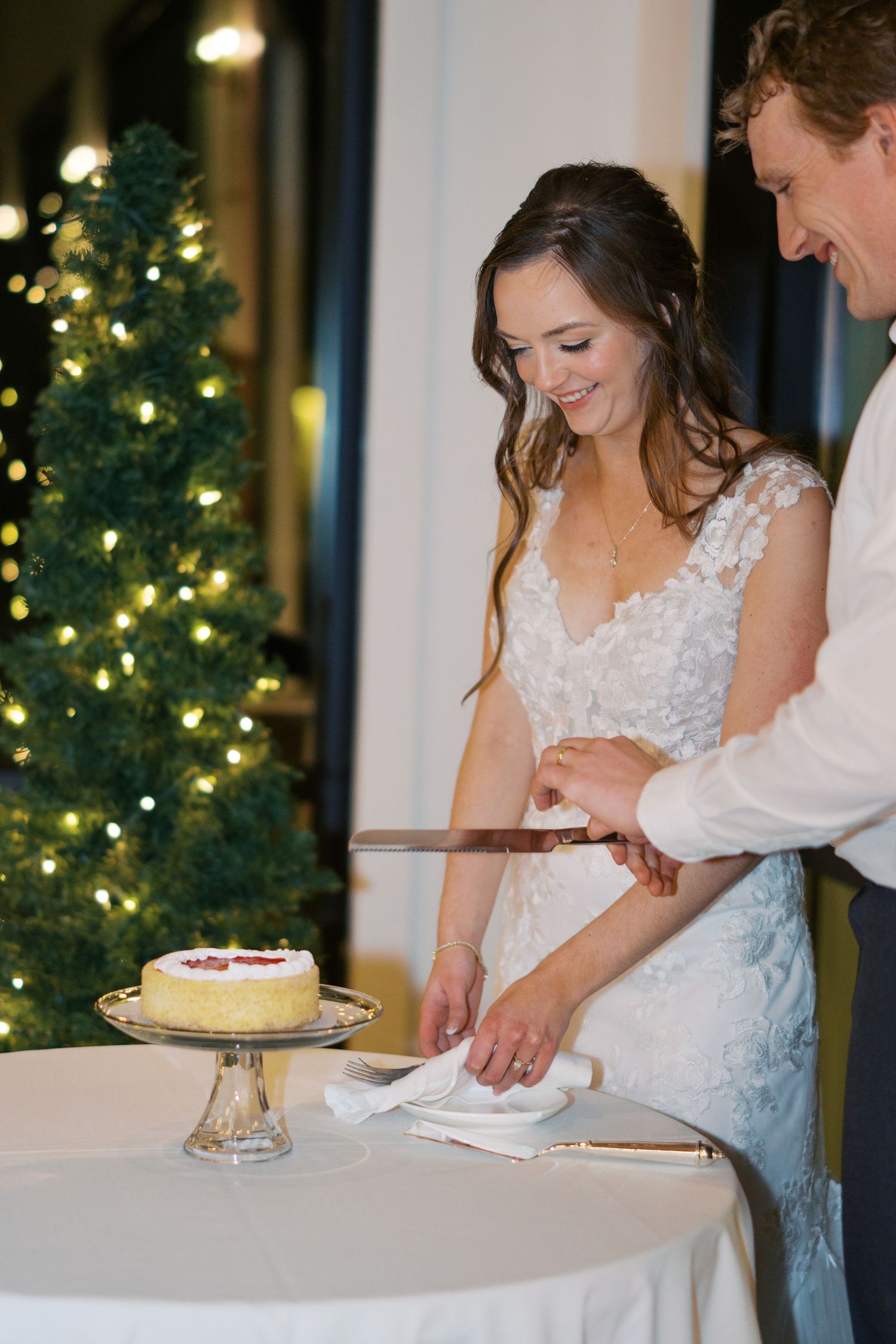 Wedding cake cutting ceremony with decorated Christmas tree in background.