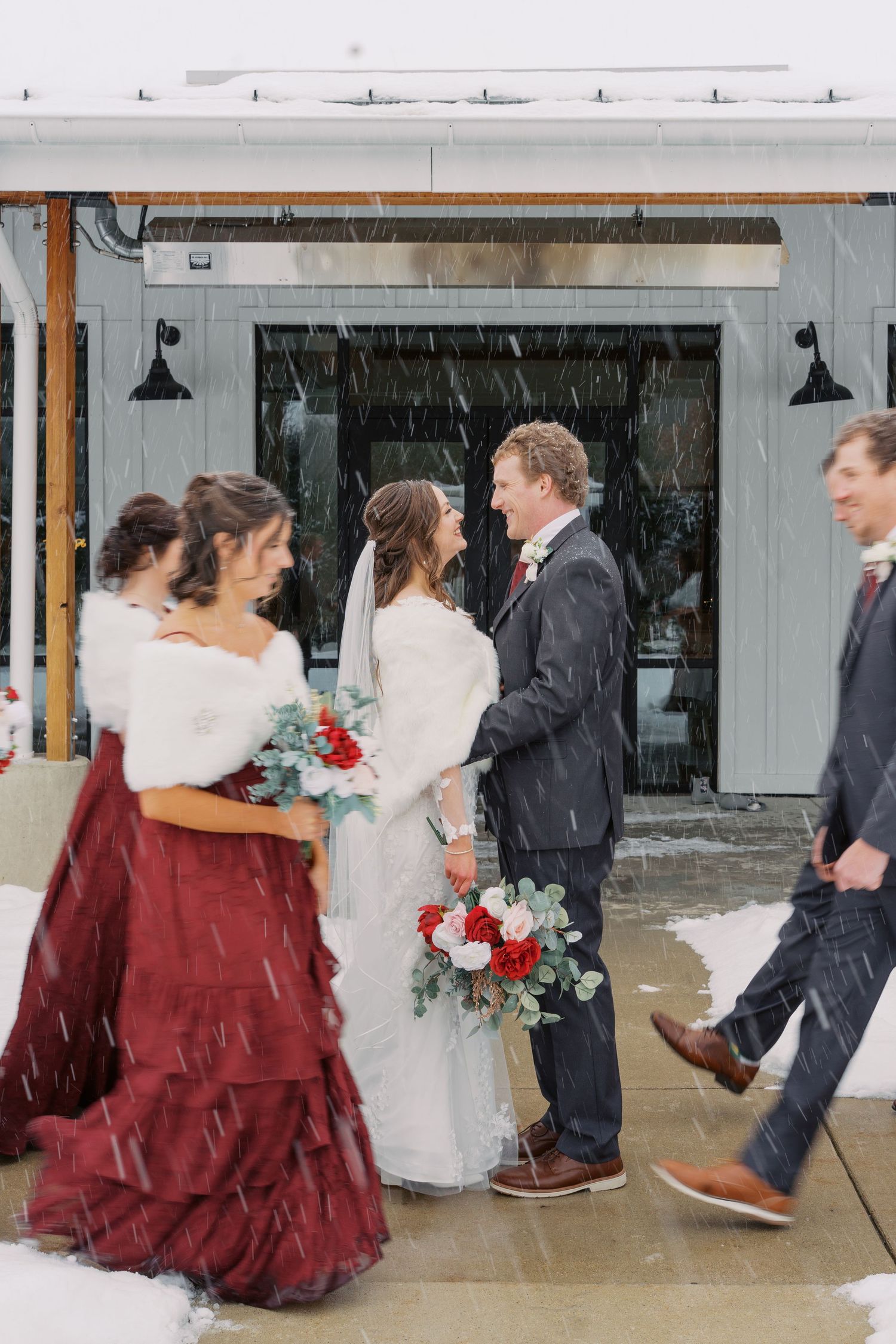 Wedding party walking together in the snow with burgundy dresses and navy suits.