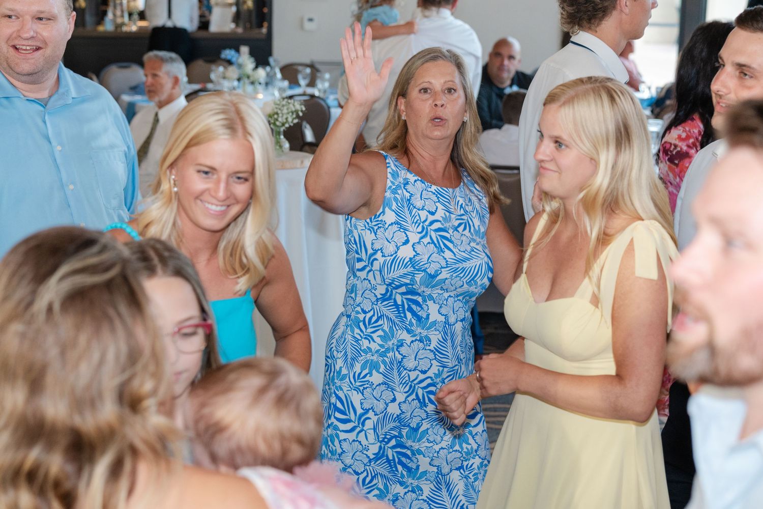 Wedding guests dancing and celebrating in summer dresses at a lively reception.