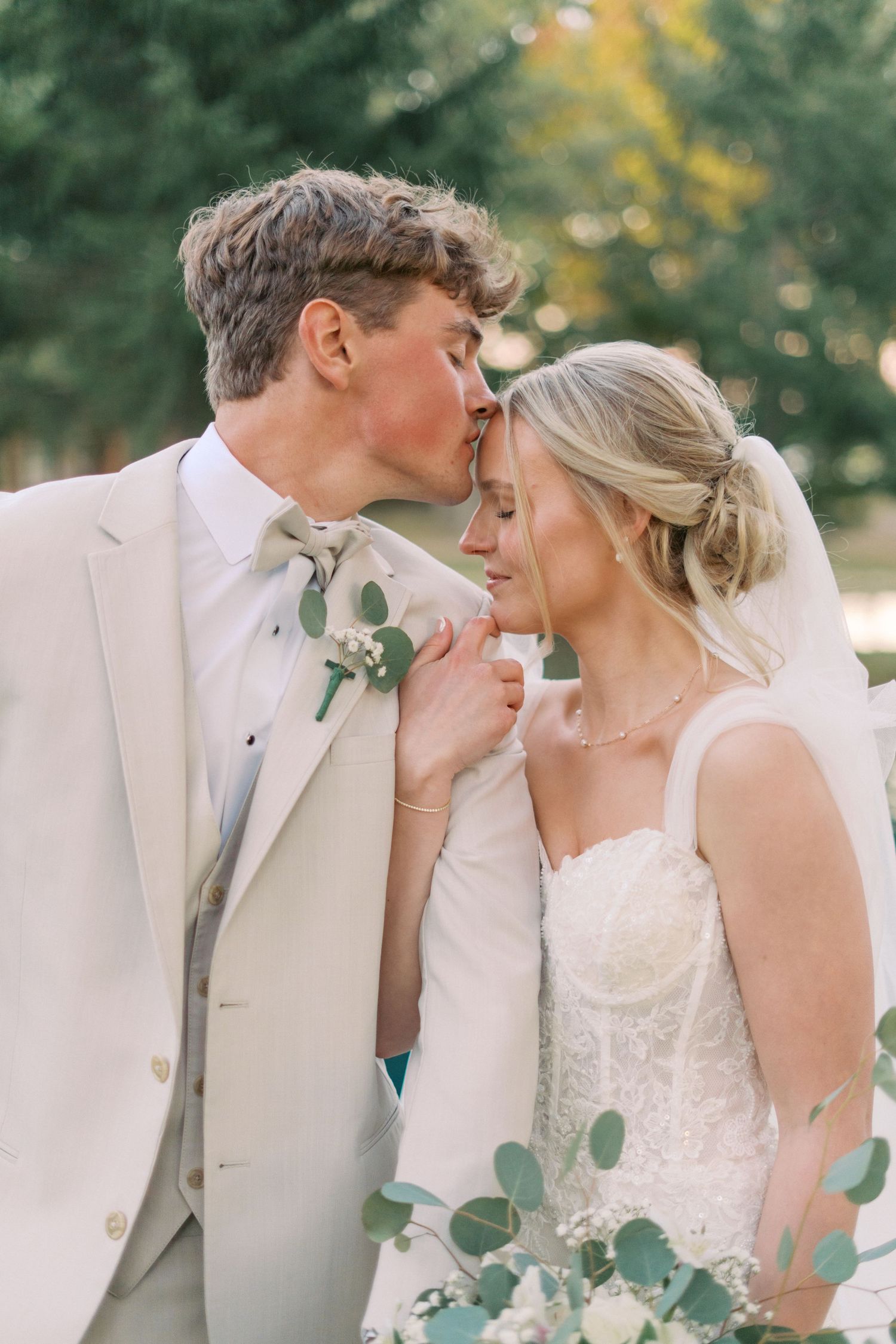 Intimate wedding portrait of couple with eucalyptus bouquet against natural outdoor backdrop.
