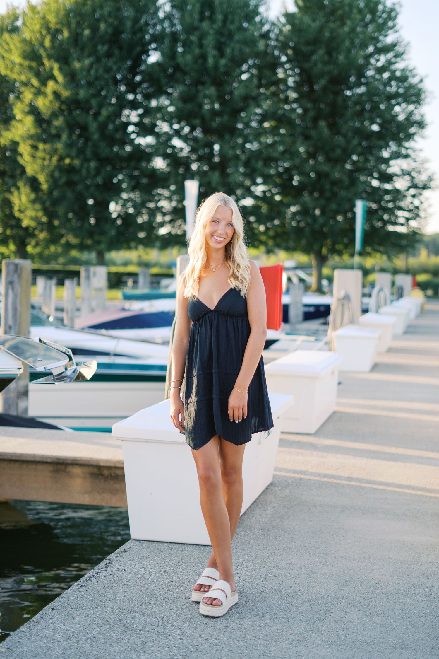 Casual summer portraits by a marina dock featuring a black dress and white sandals.