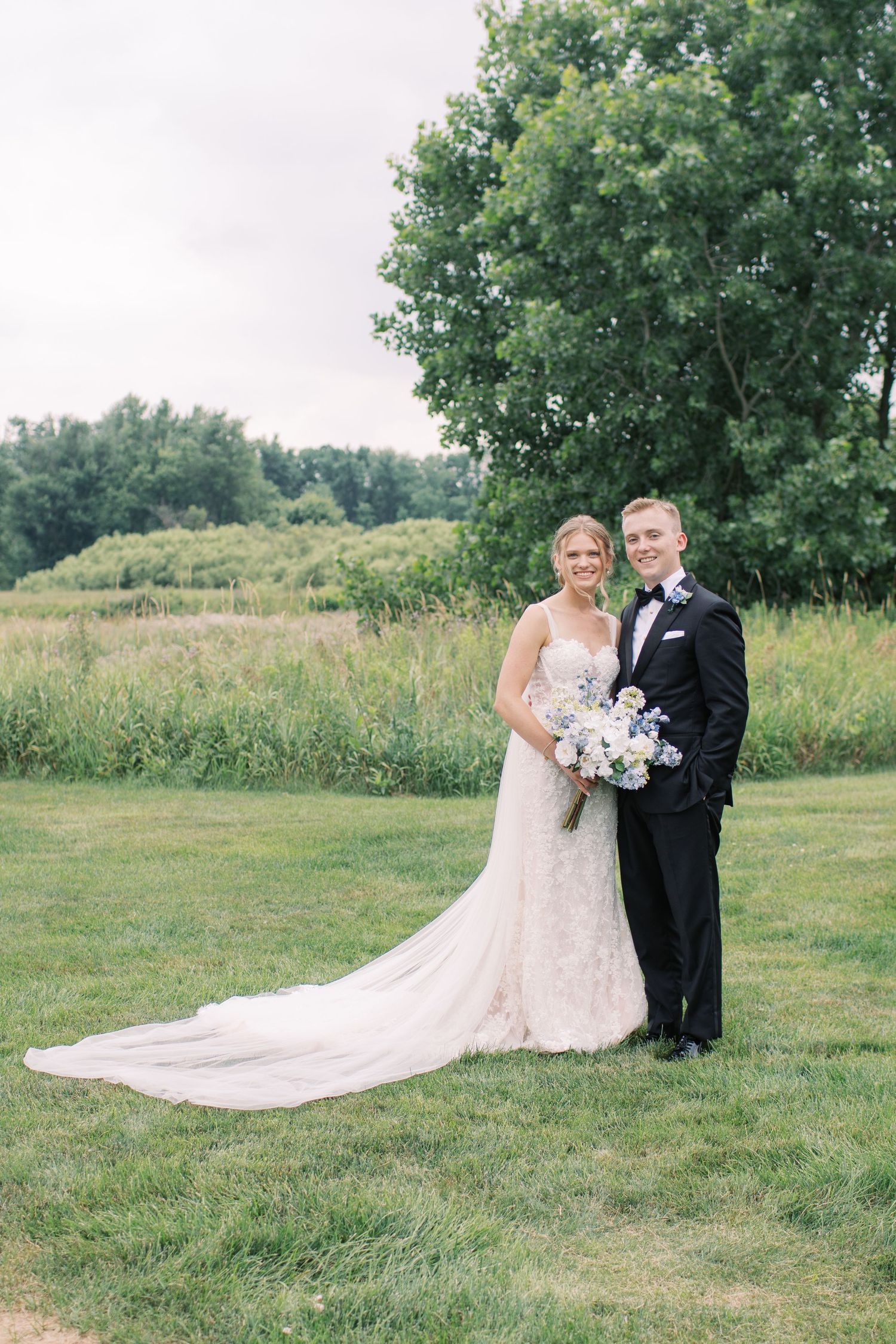 A romantic wedding photo series showing a couple in formal attire posing on a grassy hillside with trees in the background.