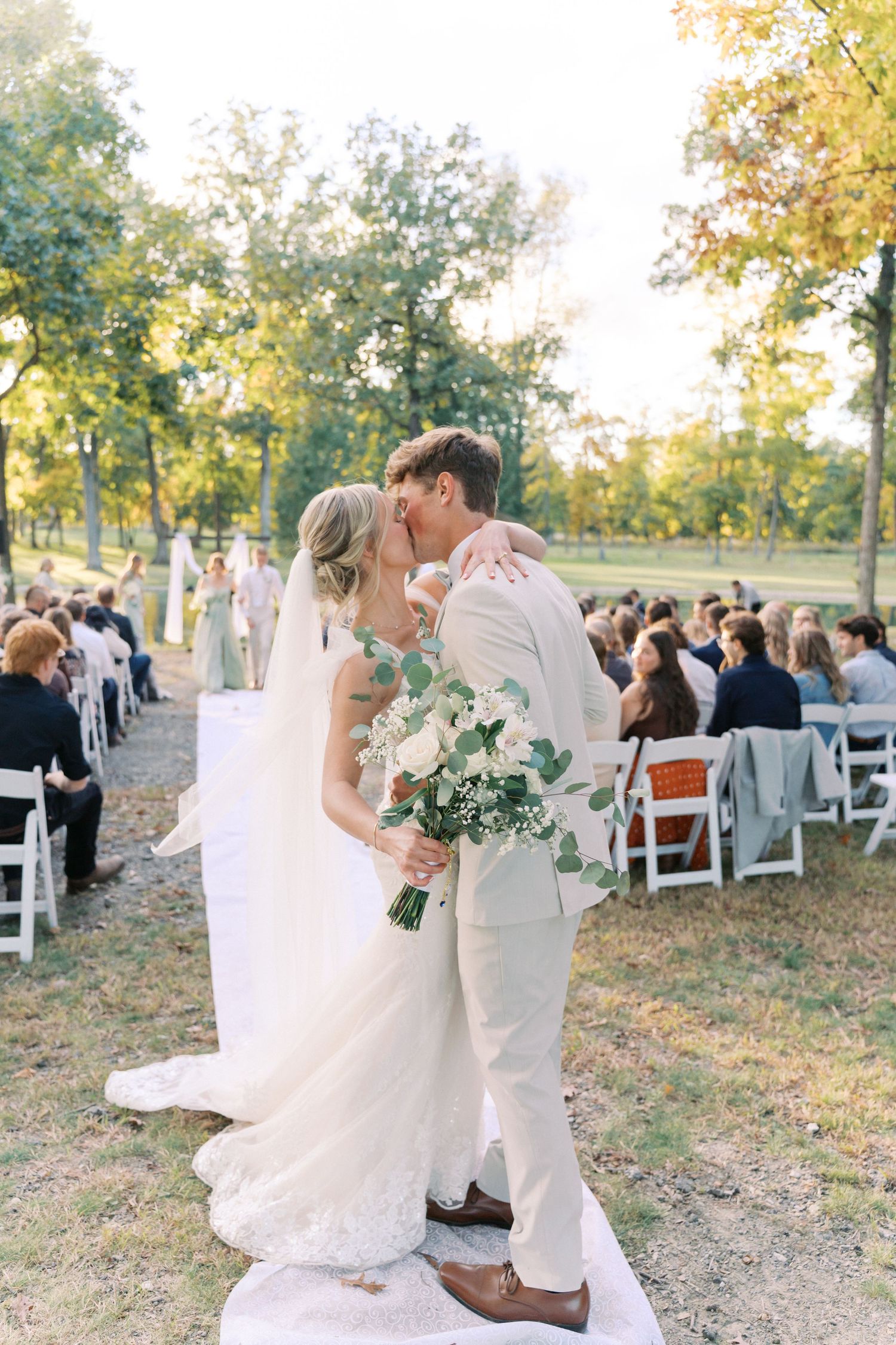 Newlyweds share romantic kiss on elevated platform during outdoor autumn ceremony.