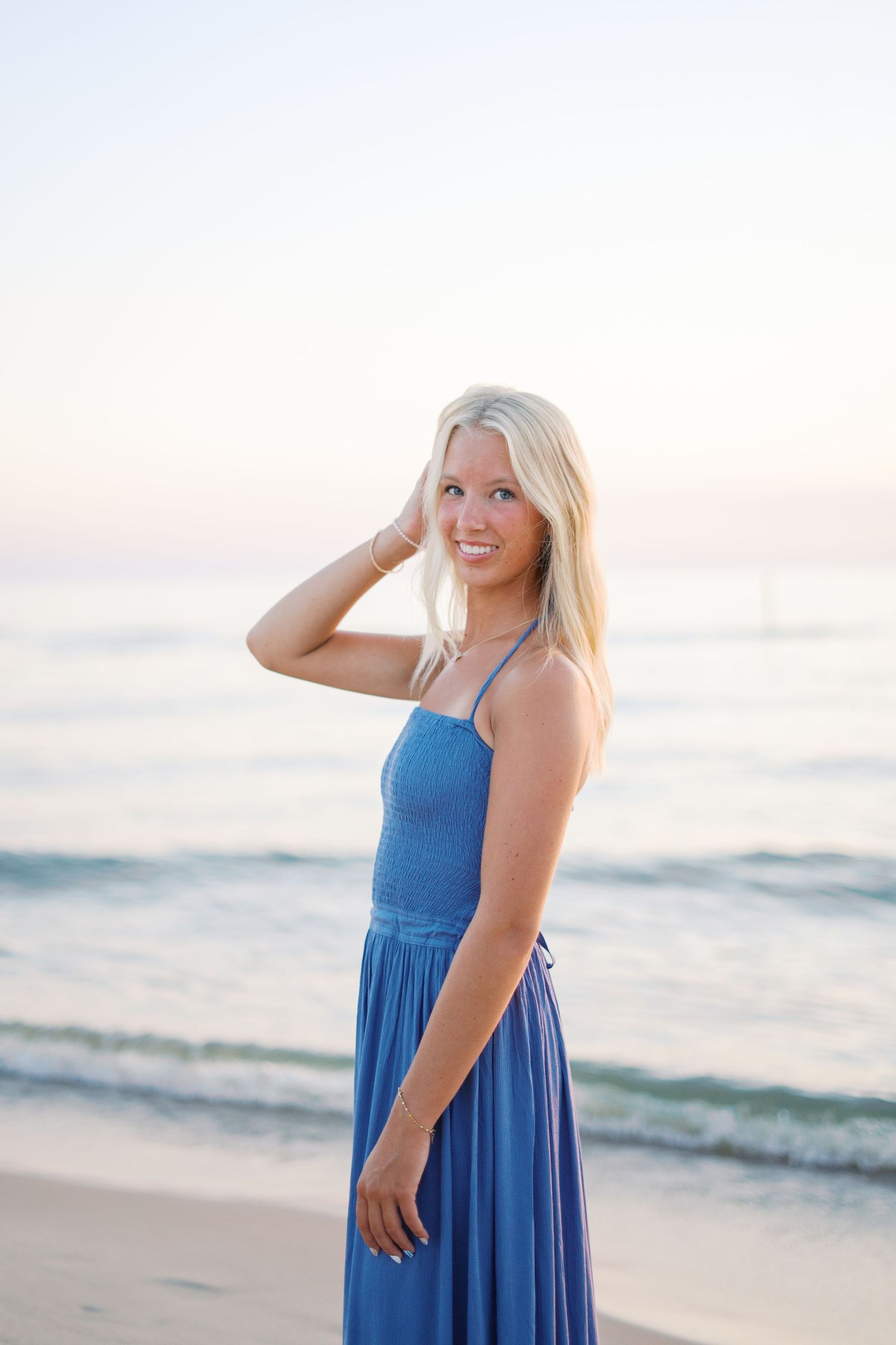 Casual beach portraits at dusk wearing a blue sundress with ocean waves in background.