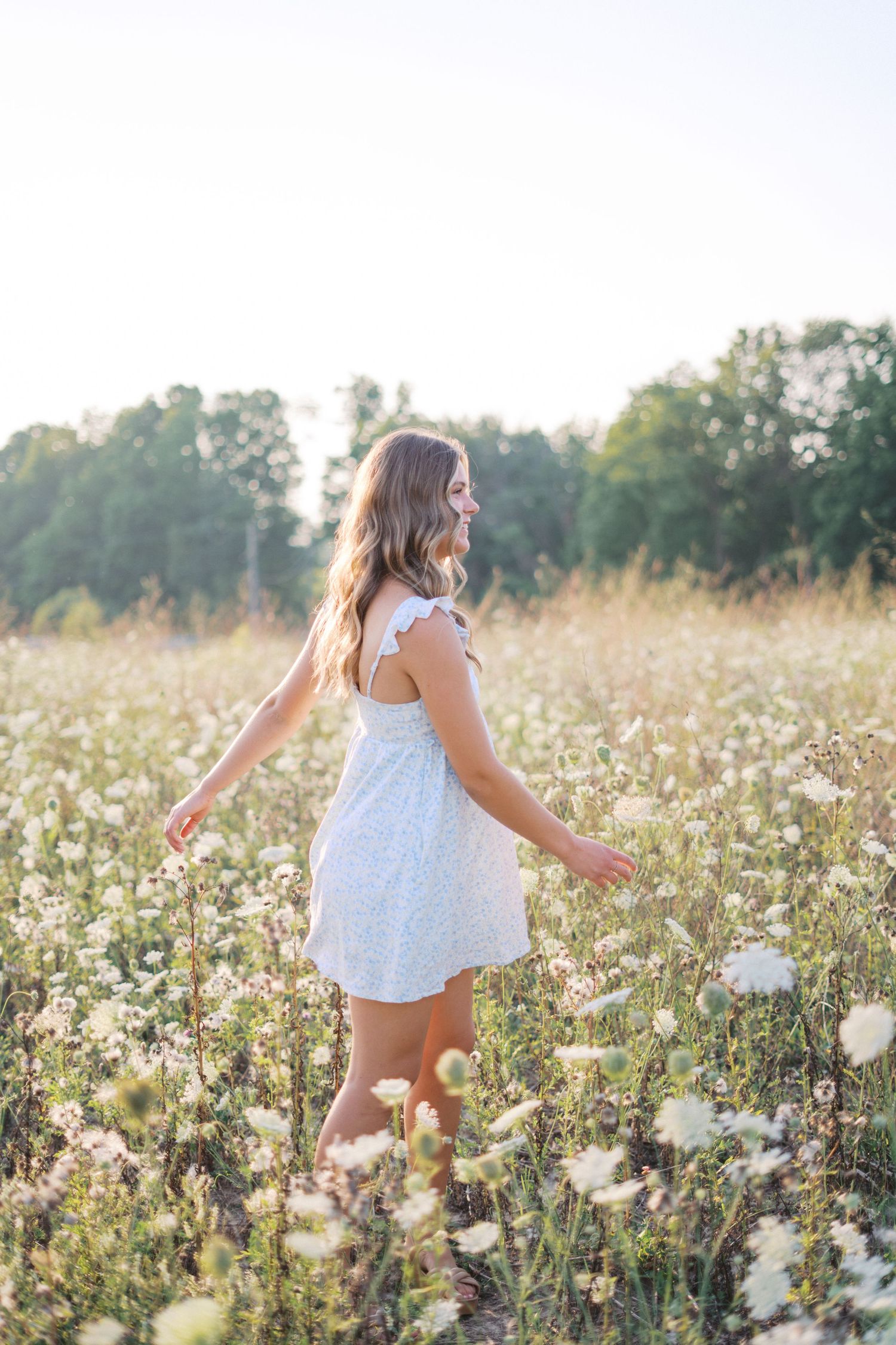 Ethereal summer scene with someone walking through a field of white wildflowers at sunset.