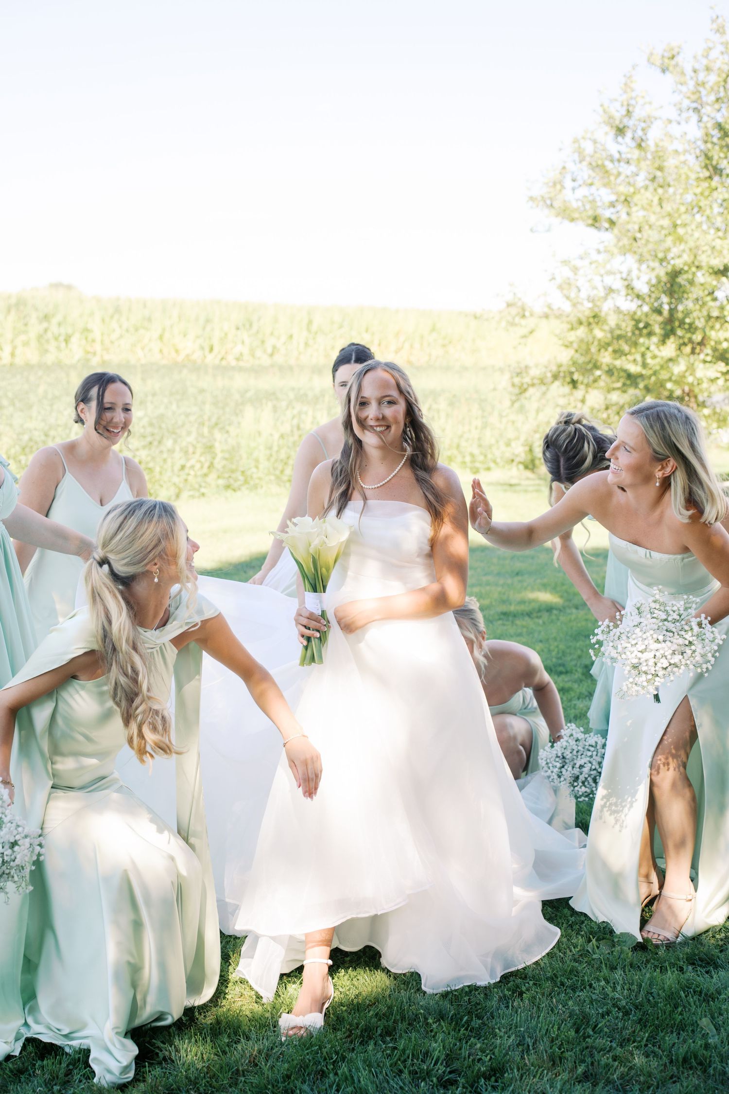 Bridesmaids in mint dresses dance and celebrate with the bride on a grassy lawn.