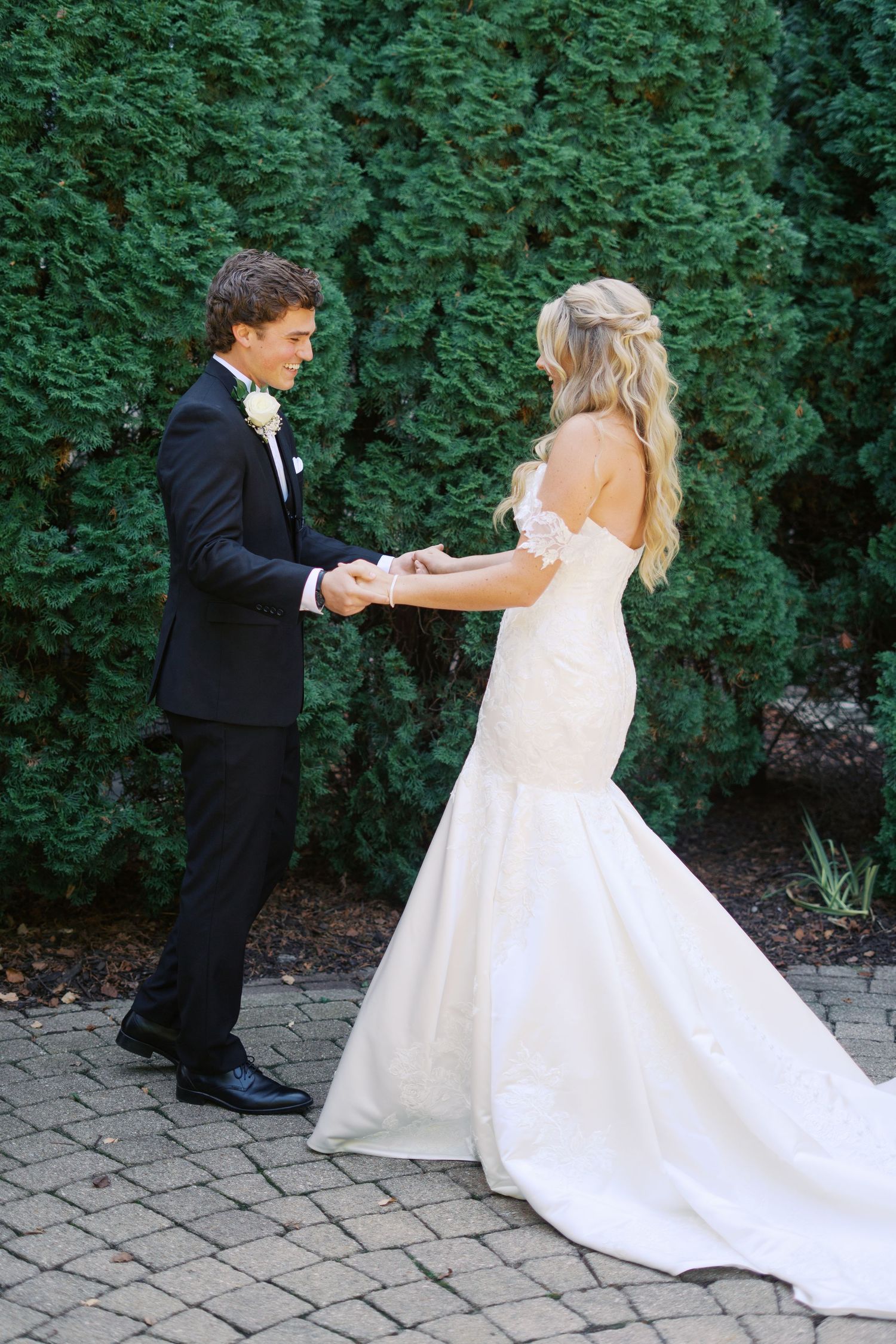 A couple in wedding attire dance and twirl together on a brick patio surrounded by greenery.