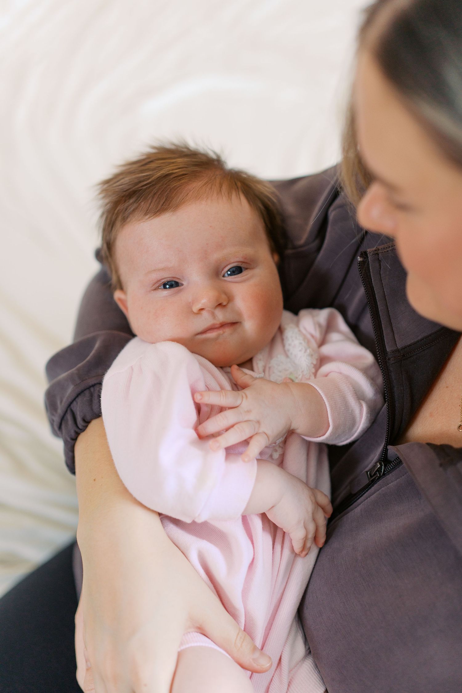 Baby in pink outfit looking at camera while being held.