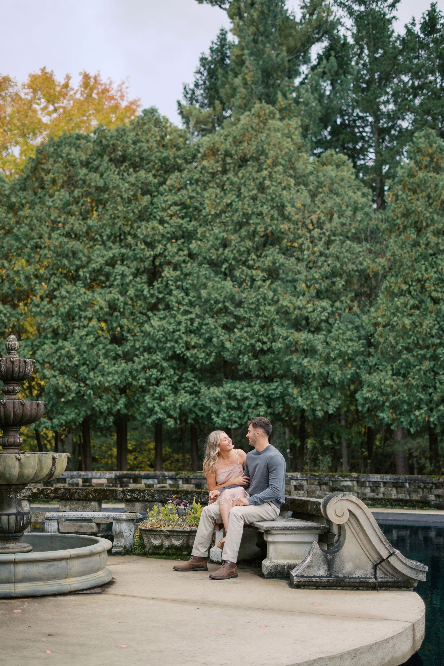 A couple sitting on ornate stone garden furniture surrounded by autumn trees.
