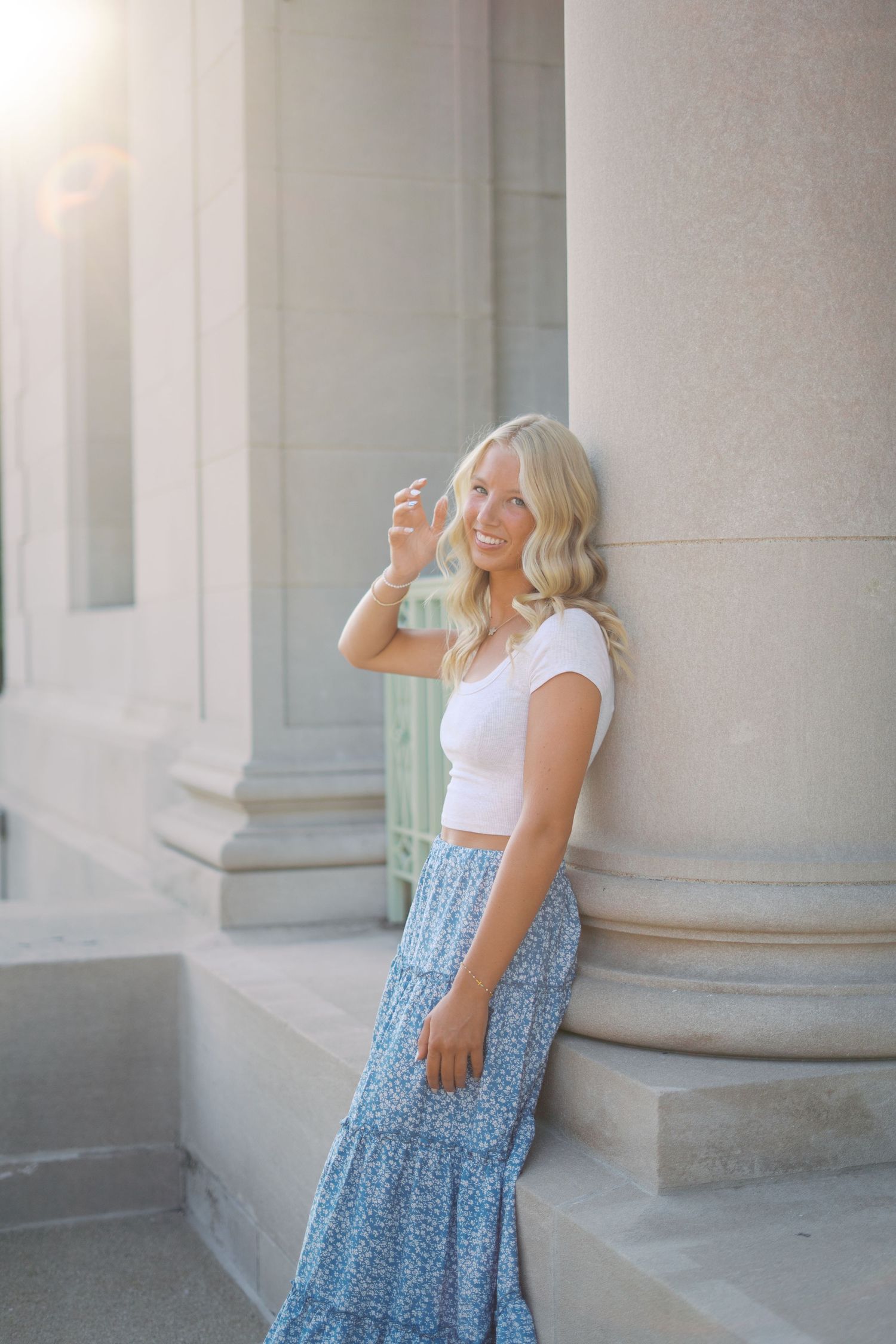 A person wearing a white tank top and blue patterned skirt poses playfully by stone pillars.