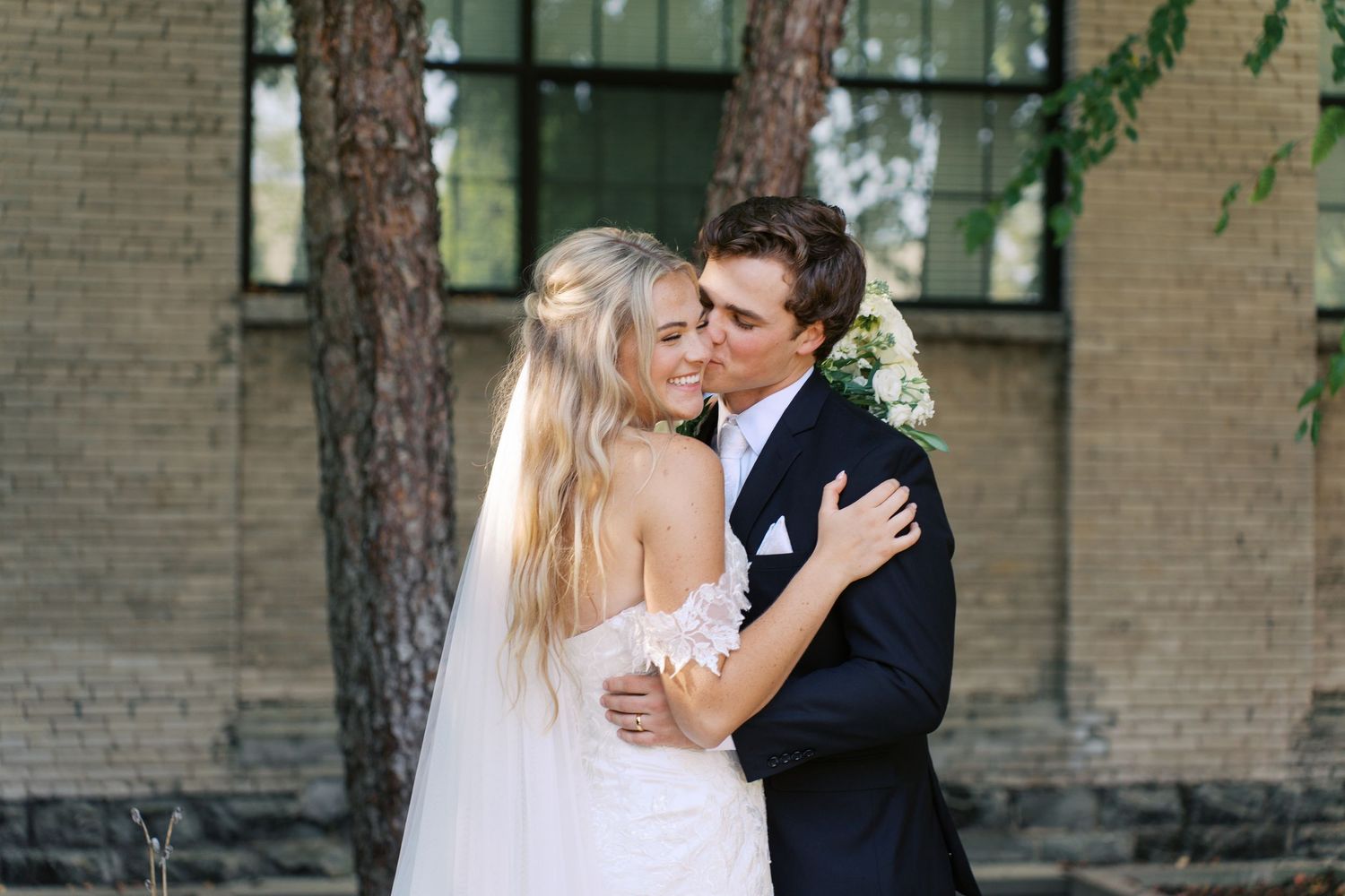 A romantic wedding couple shares an intimate moment against a brick building.