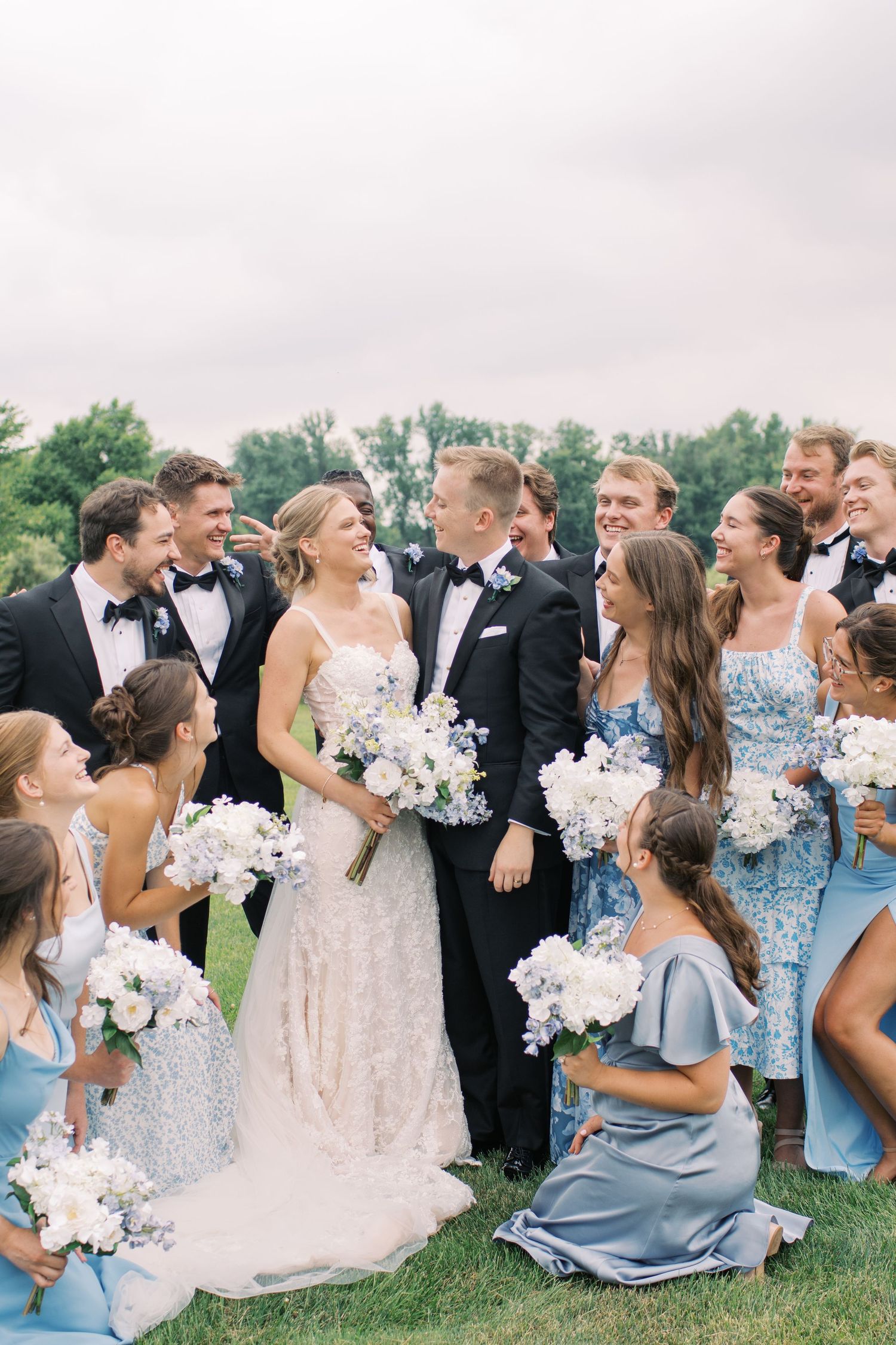 Wedding party in light blue bridesmaid dresses and formal attire celebrates joyfully outdoors.