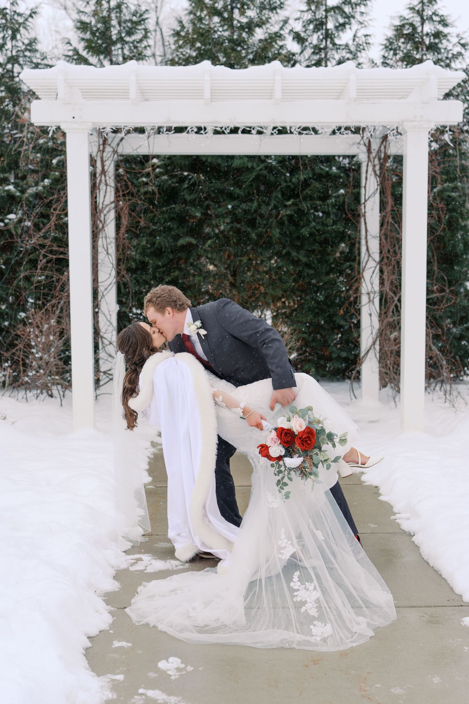 Romantic dip kiss under white wedding arbor surrounded by snow.