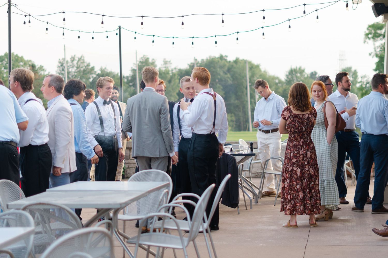 Wedding guests mingling on an outdoor patio decorated with string lights at dusk.