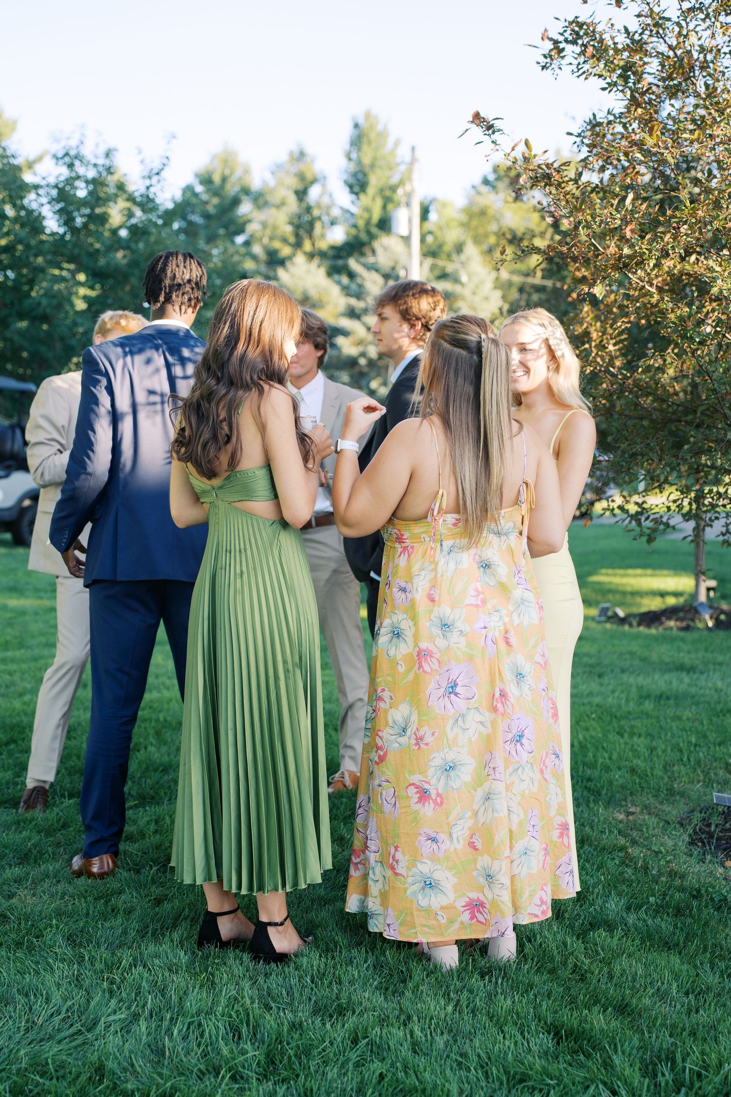Wedding guests in colorful summer dresses chatting on manicured lawn.