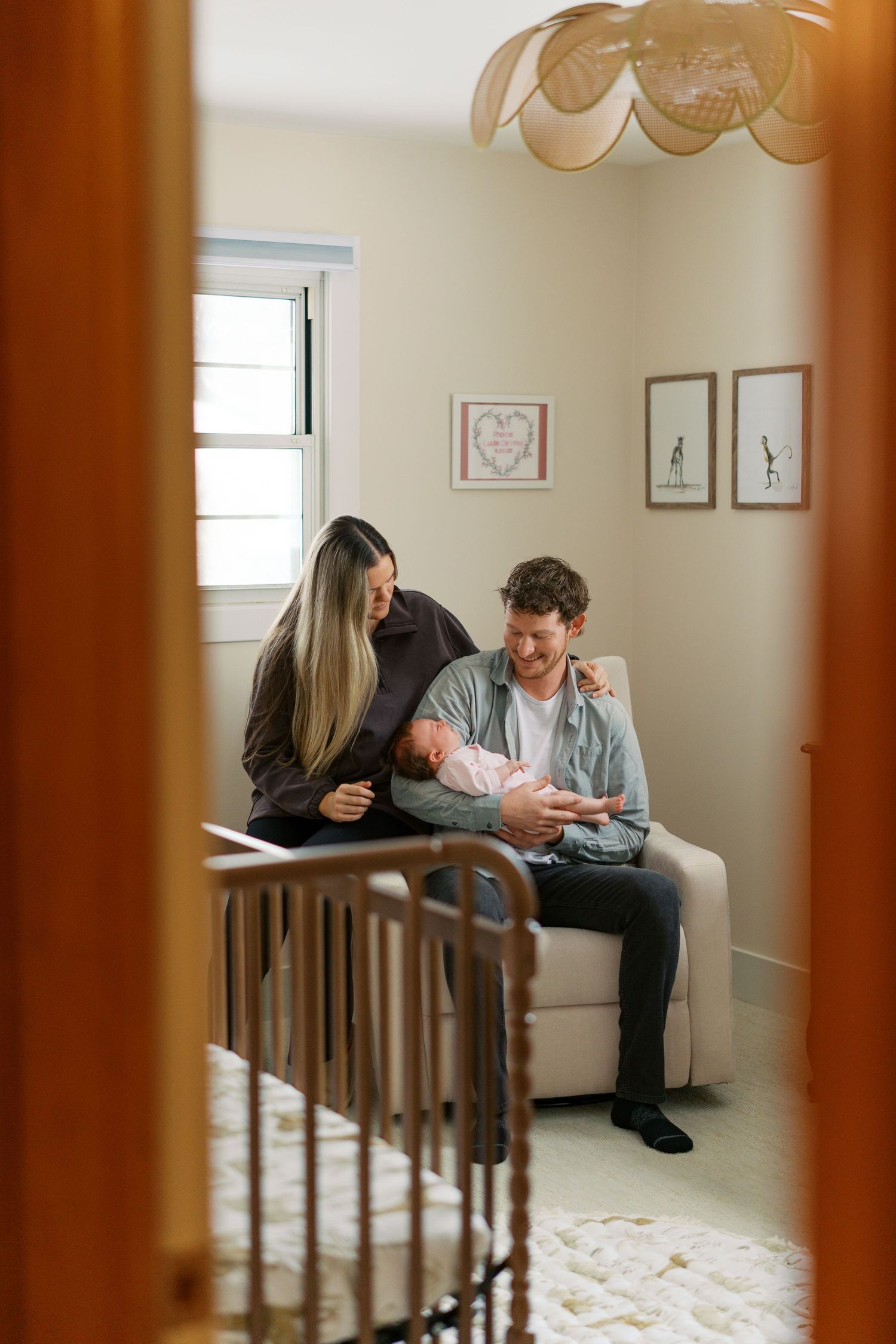 A nursery room view through wooden crib bars showing a couple sitting on a couch.