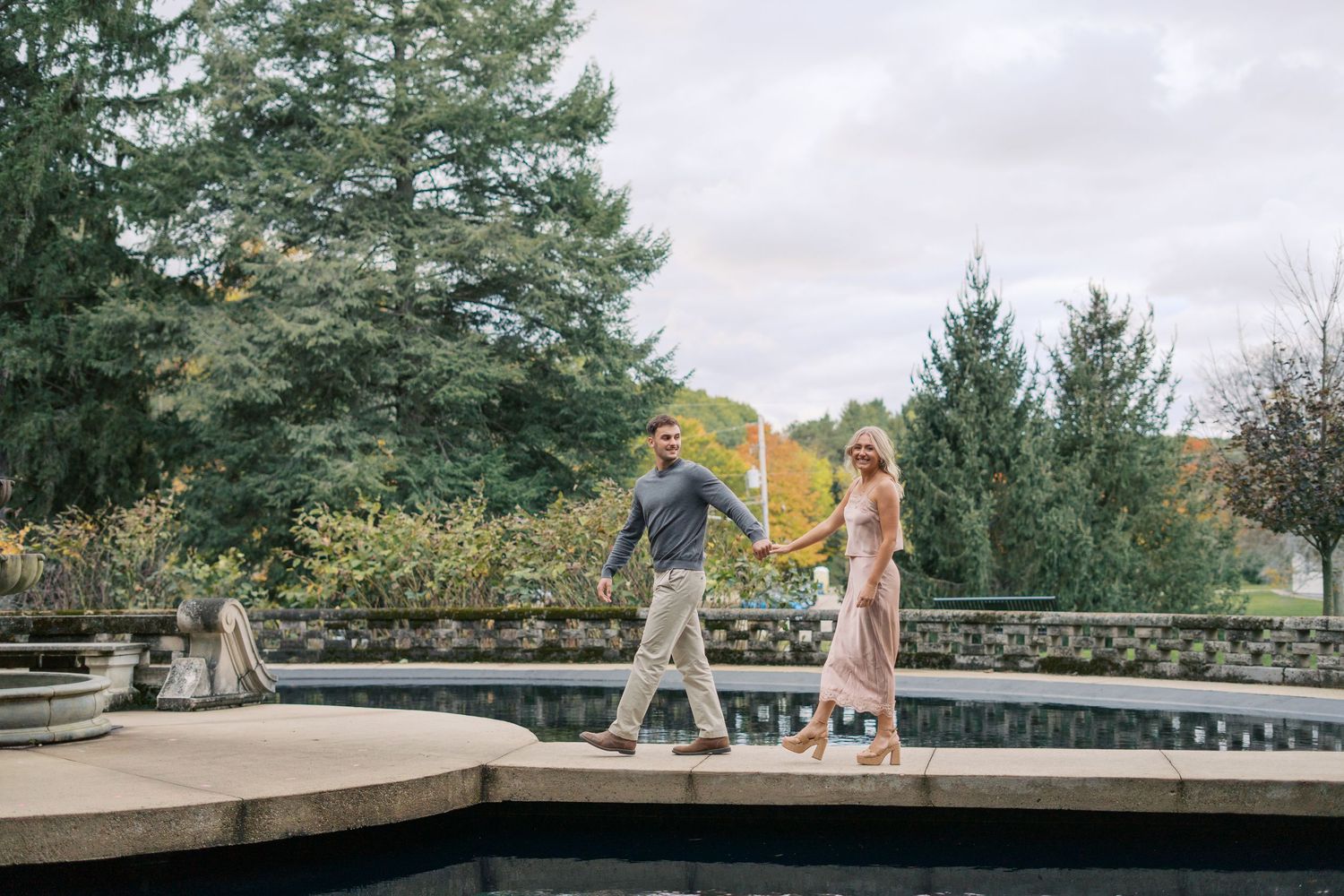 A couple walking together on a curved stone pathway surrounded by evergreen trees.