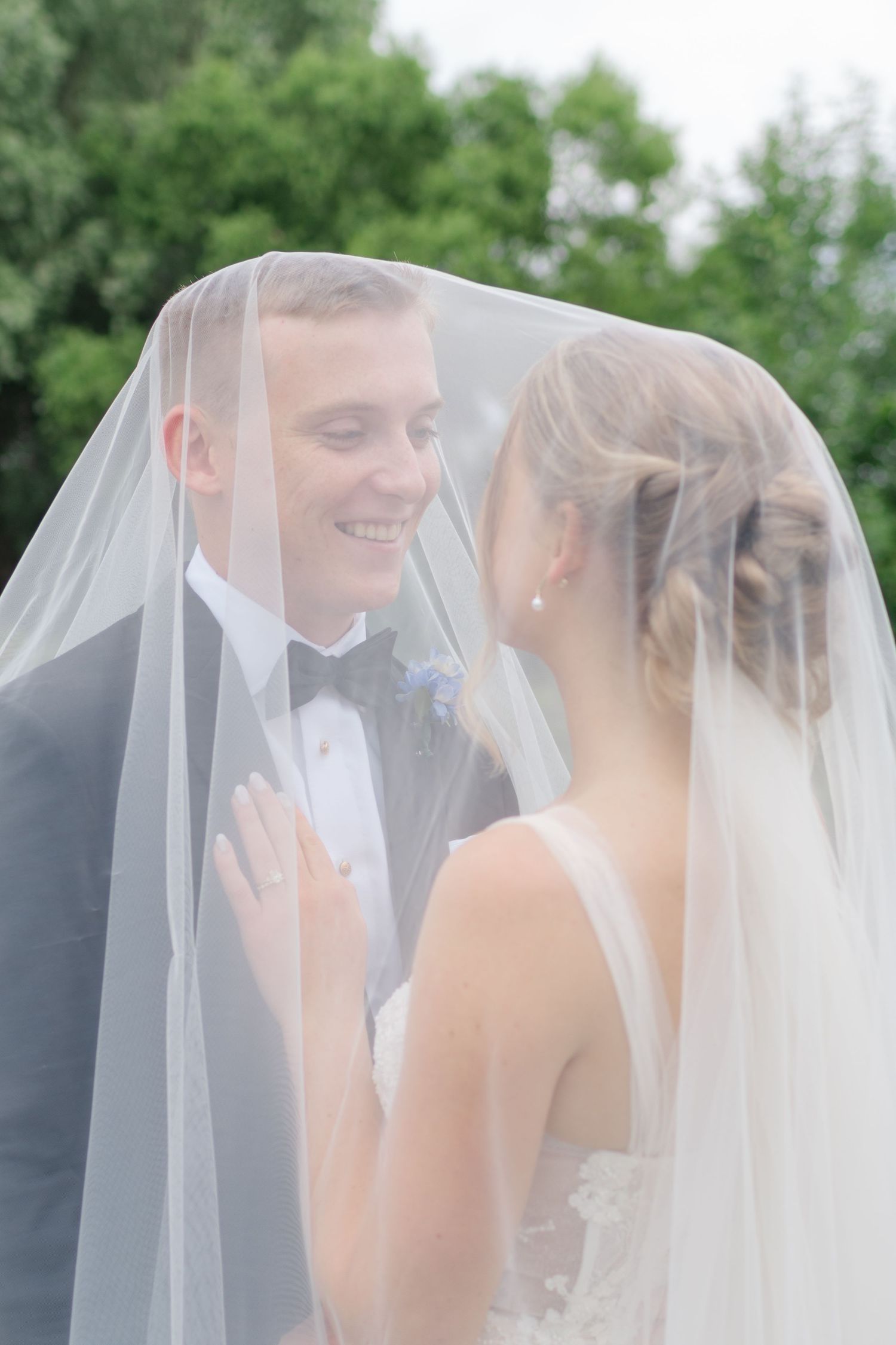 Romantic moments shared under a flowing wedding veil against natural outdoor scenery.
