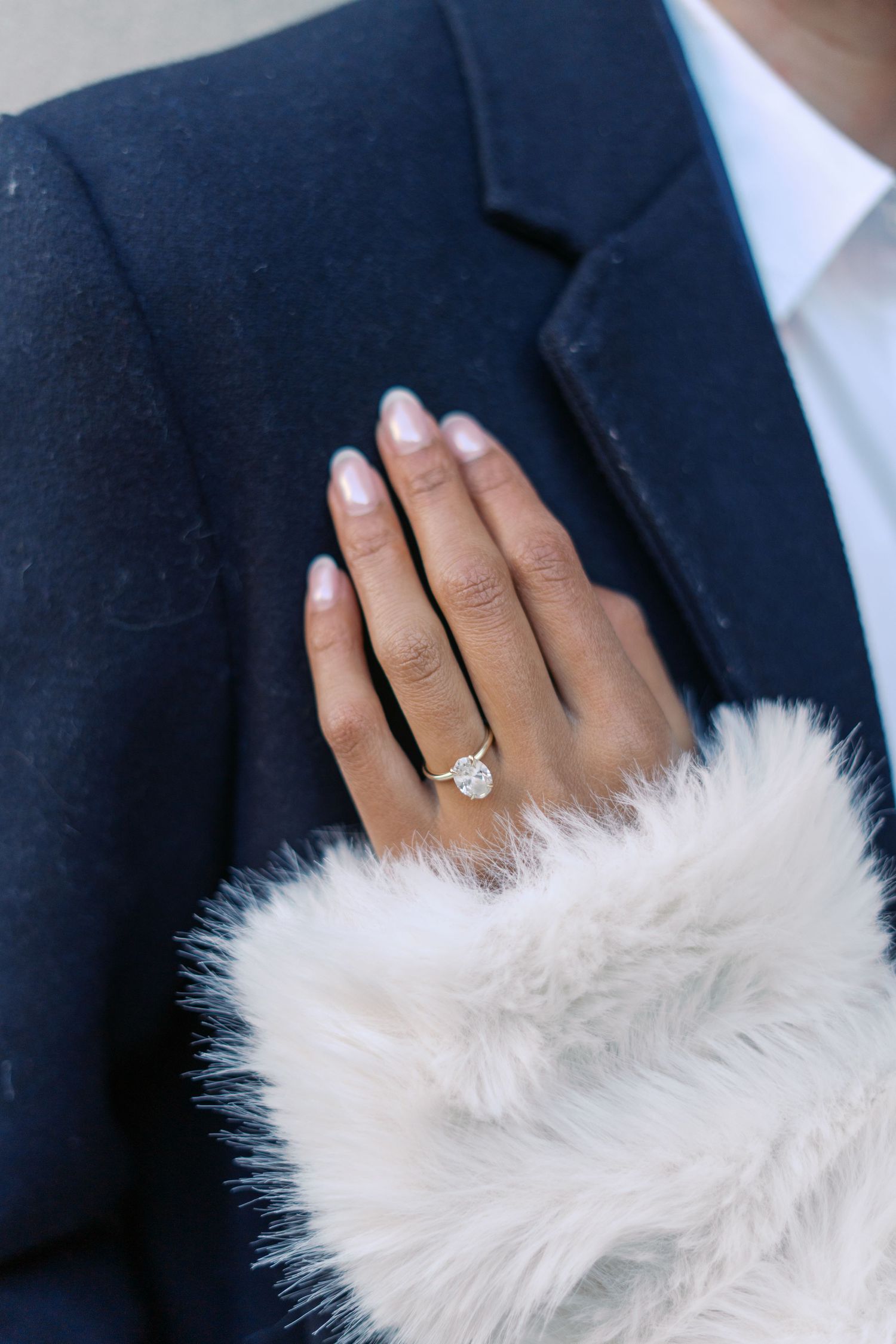 Close-up of engagement ring with white fur wrap detail against navy suit.