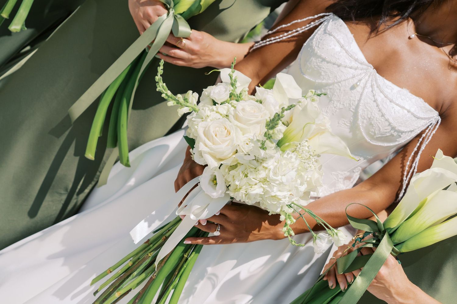 Bride in white gown holding elegant white rose and lily bouquet with green stems at a wedding ceremony.