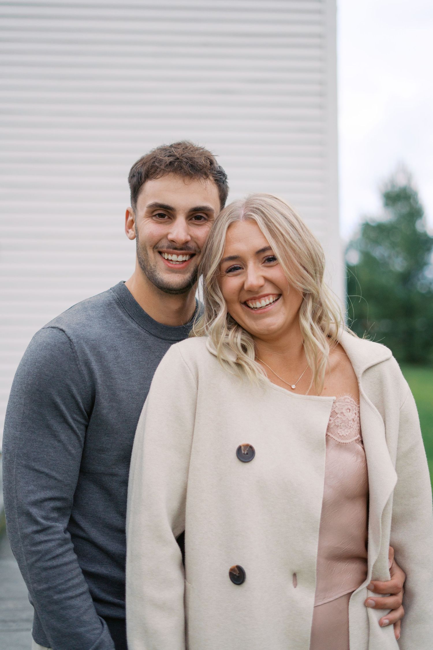 A joyful couple laughs together while wearing coordinated neutral-toned outfits.