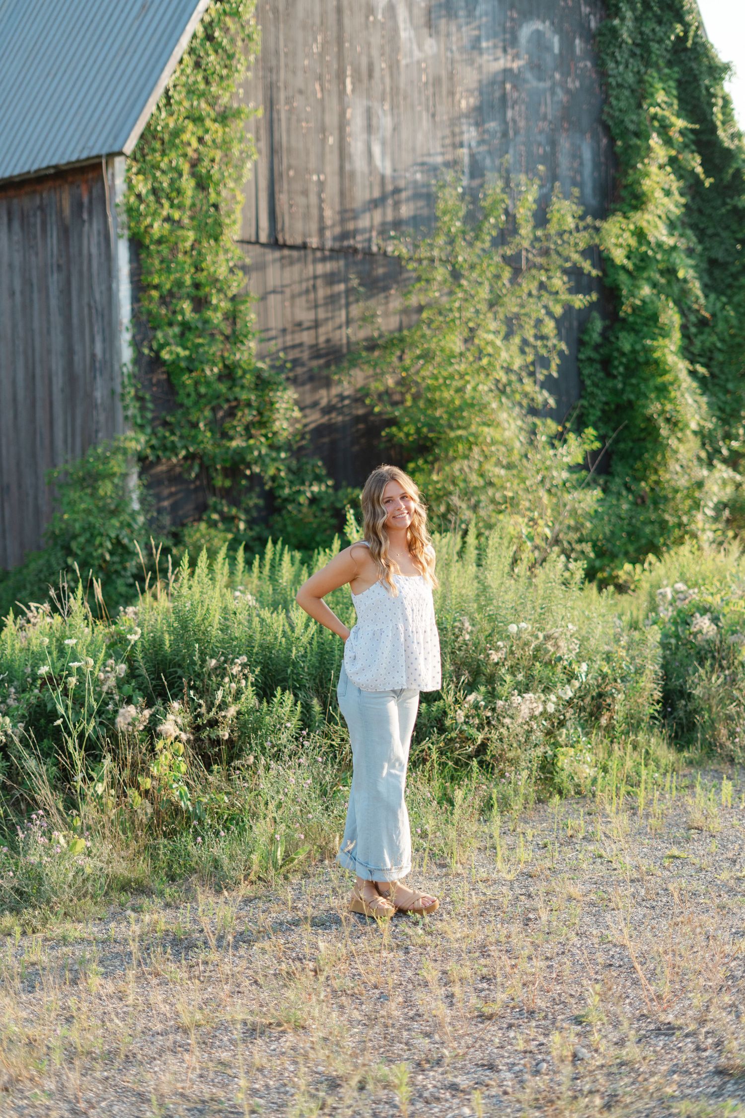 Full length portraits in a white summer dress against a rustic barn and wild grass landscape.
