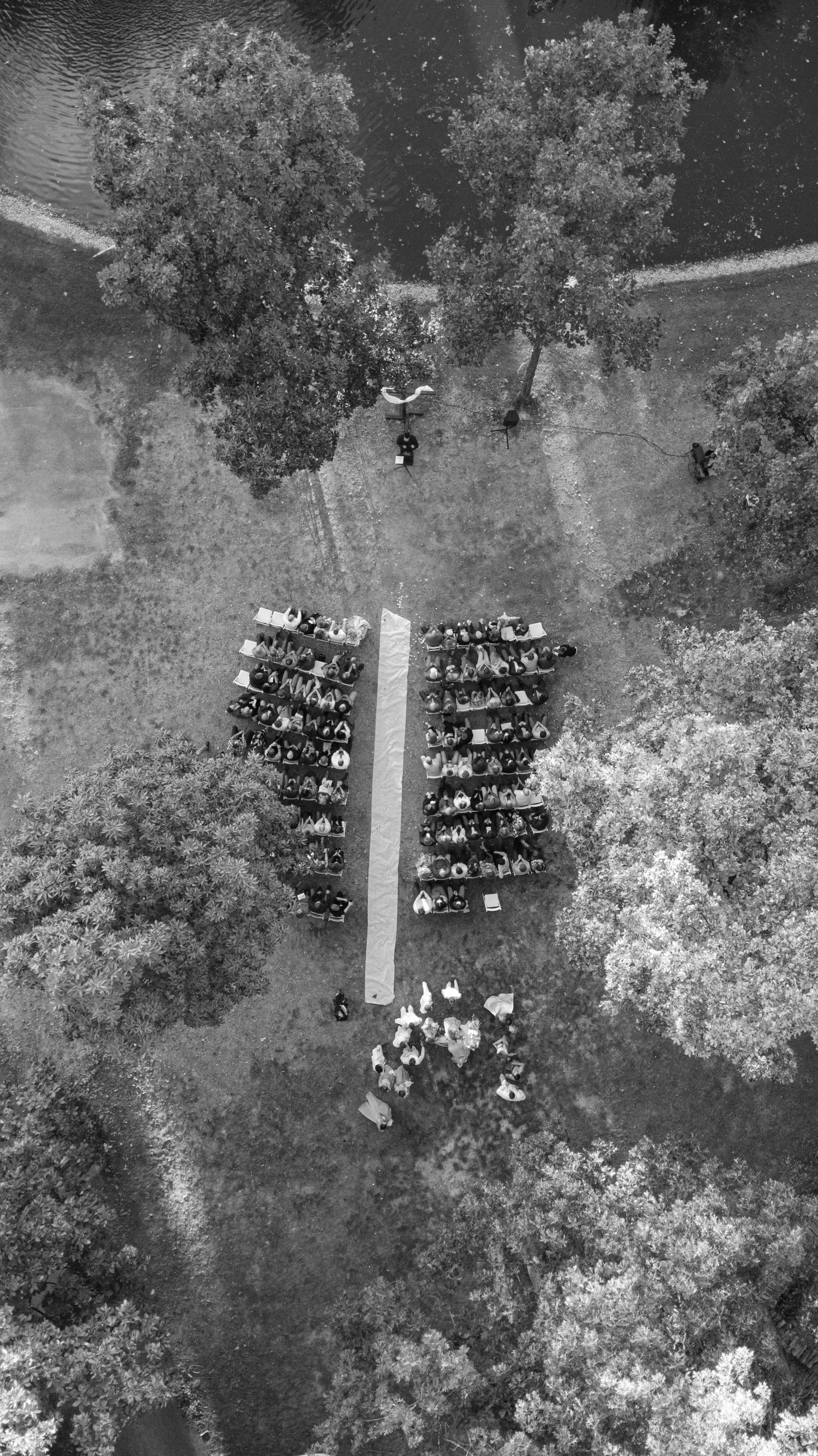Aerial black and white view of wedding guests arranged in a heart shape formation outdoors.