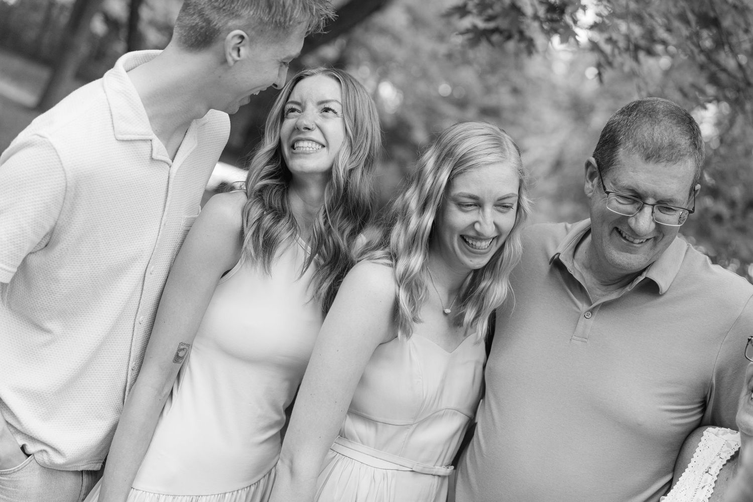 Black and white family portrait of four people laughing outdoors, capturing a joyful candid moment together.