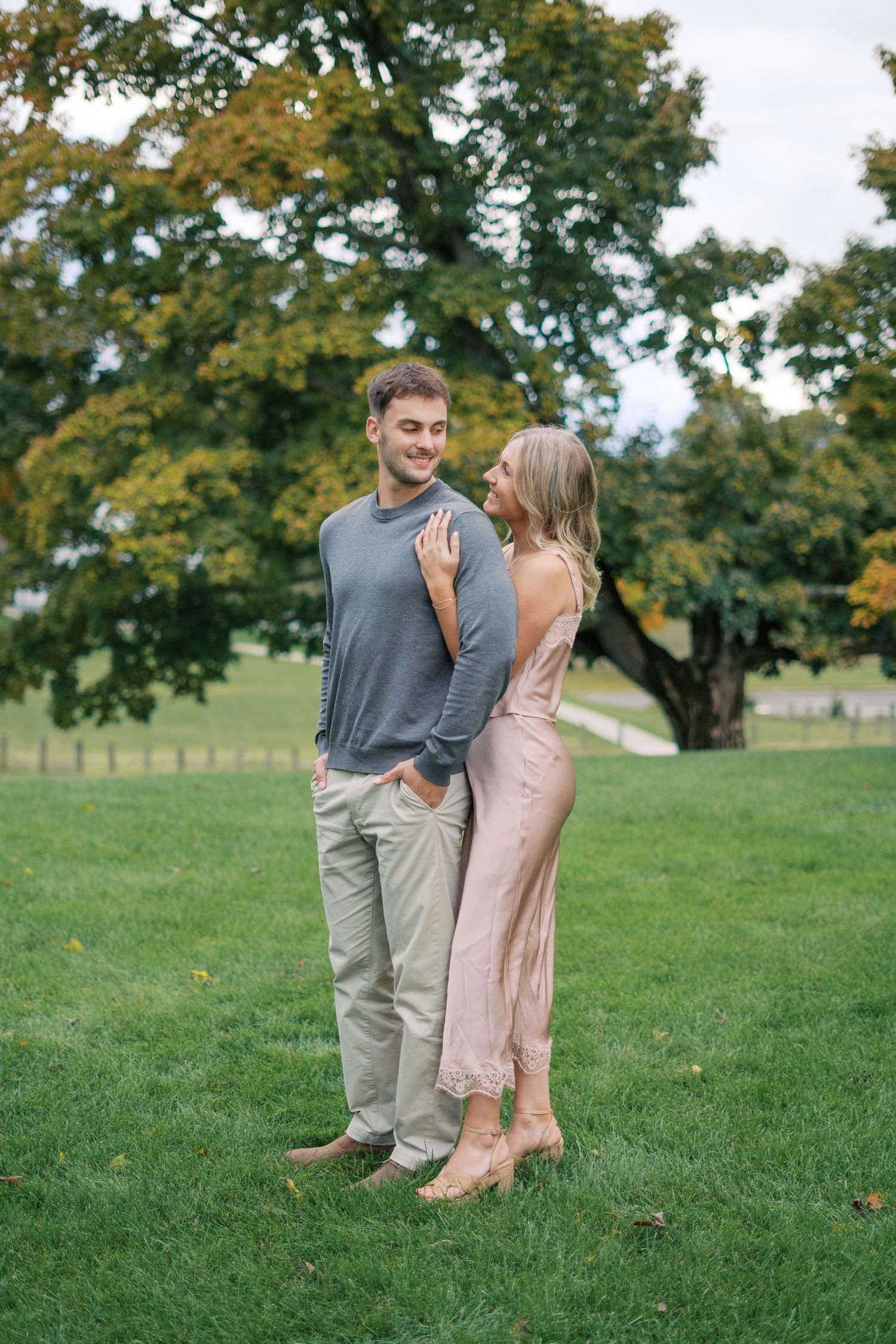 A couple in casual attire sharing an intimate moment on a grassy lawn with fall foliage.