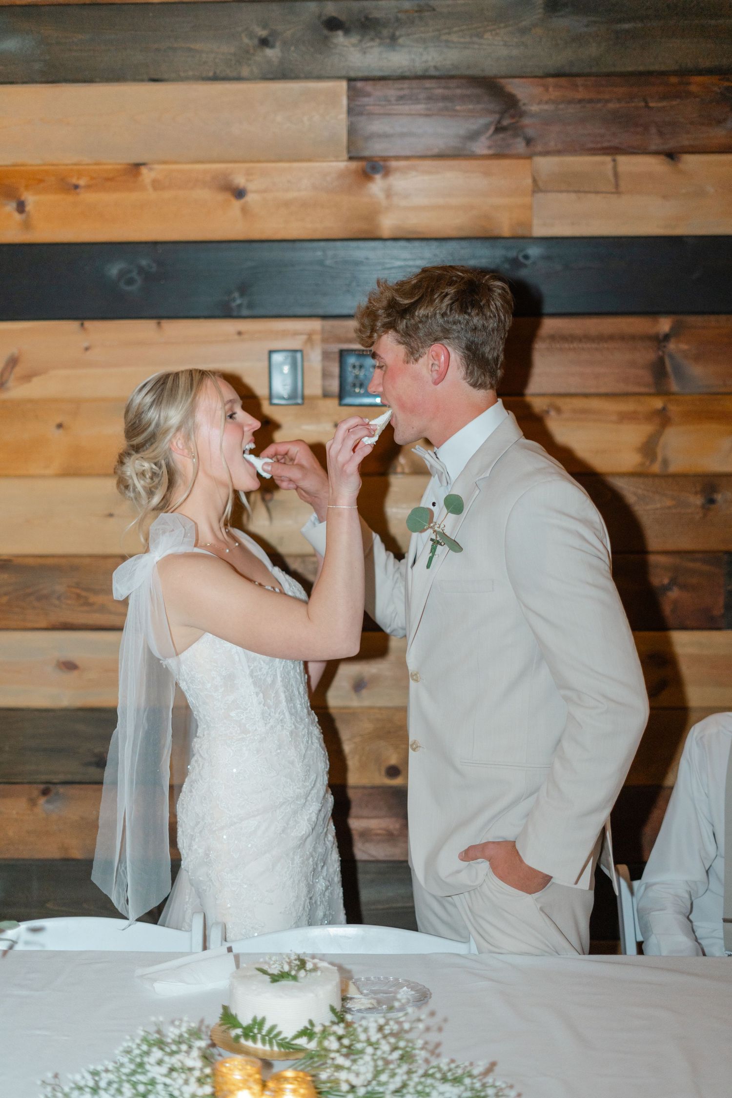 Wedding couple sharing an intimate cake-feeding moment in a rustic wooden venue.