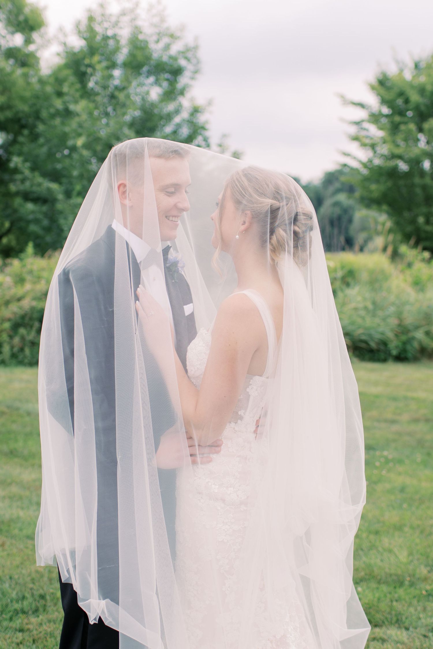 Ethereal wedding portraits with a flowing veil creating intimate moments between the newlyweds in a garden setting.
