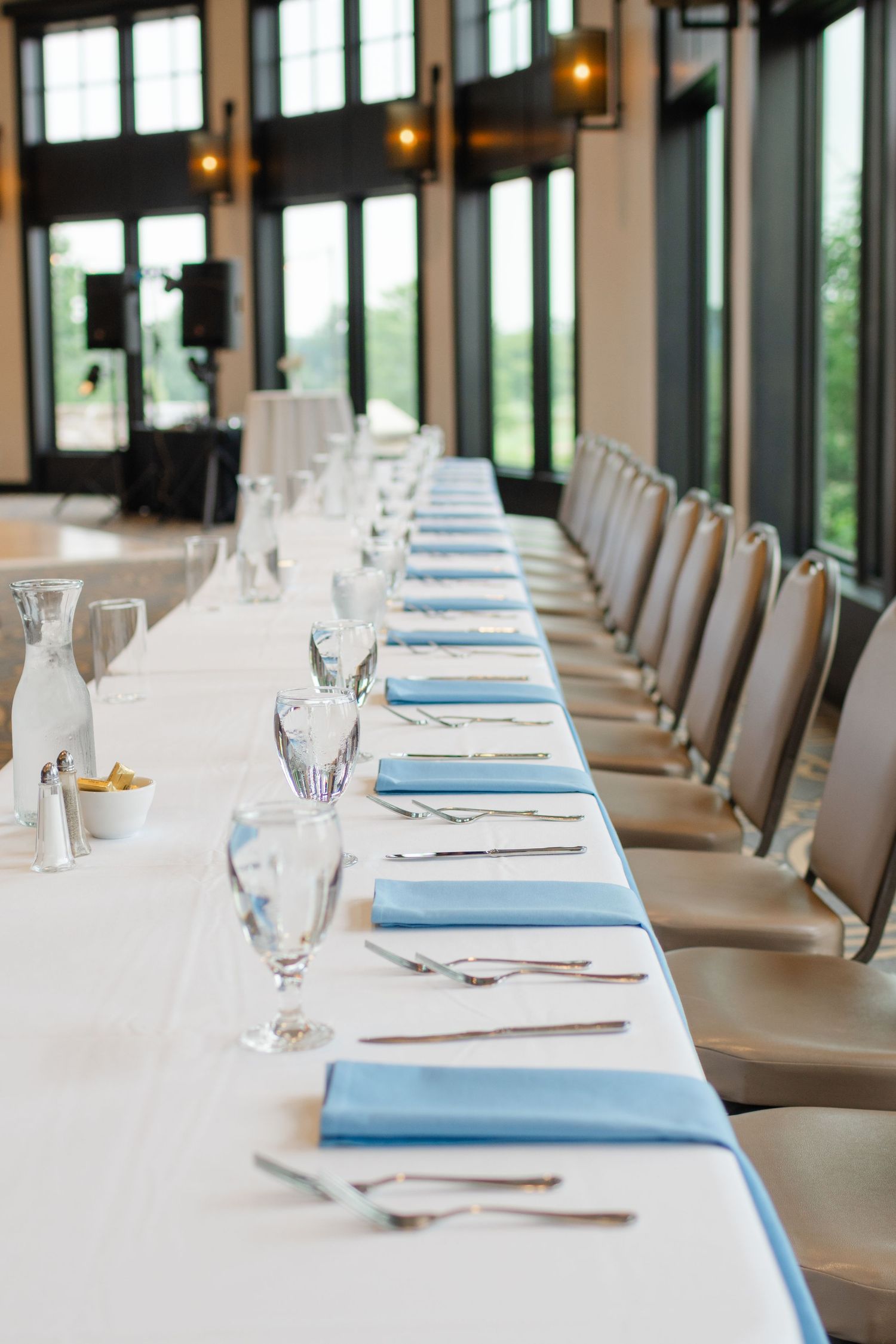 Long banquet table set with white linens, blue napkins, and elegant place settings for a formal reception.