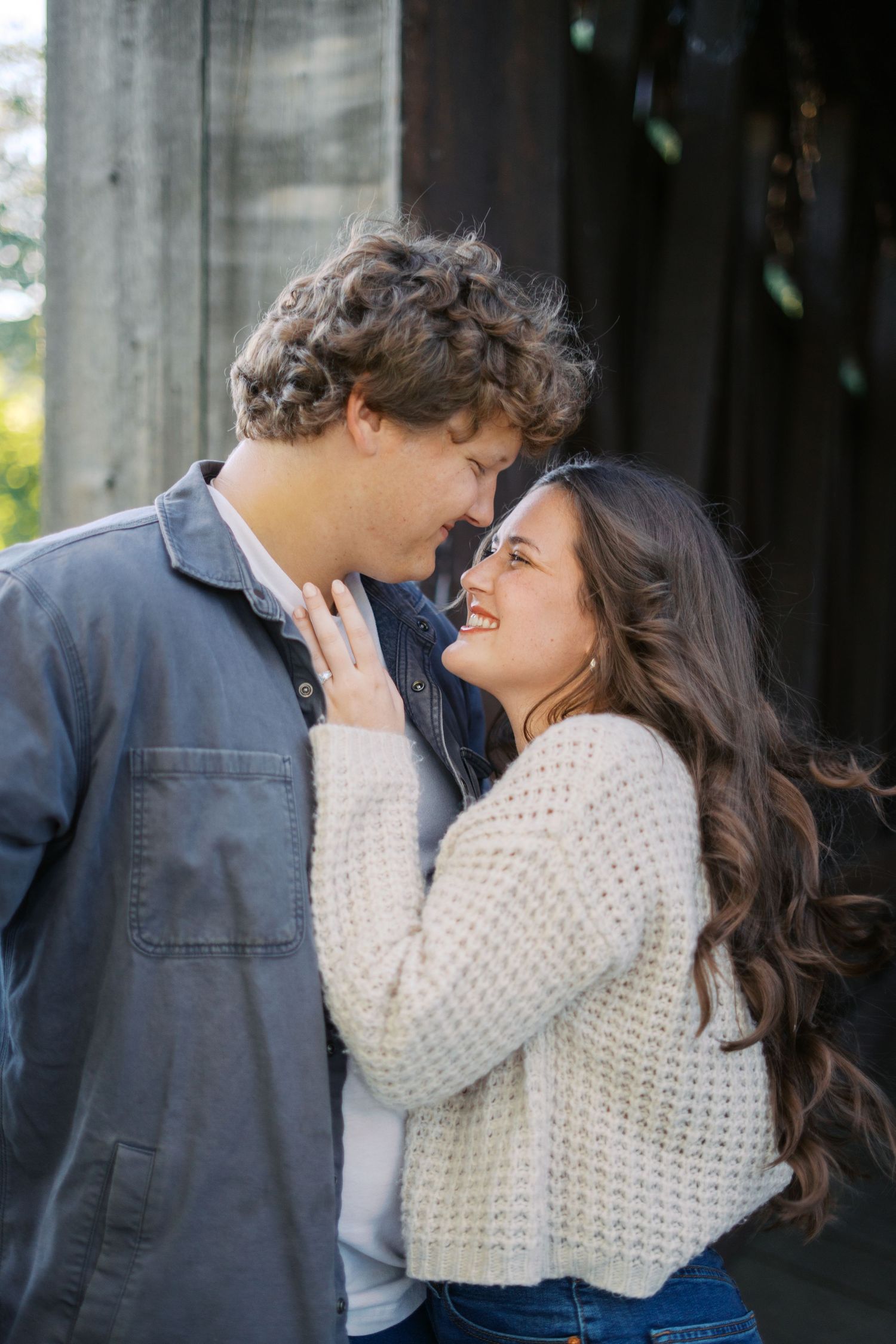 Romantic couple in casual attire sharing intimate moments under wooden structure.