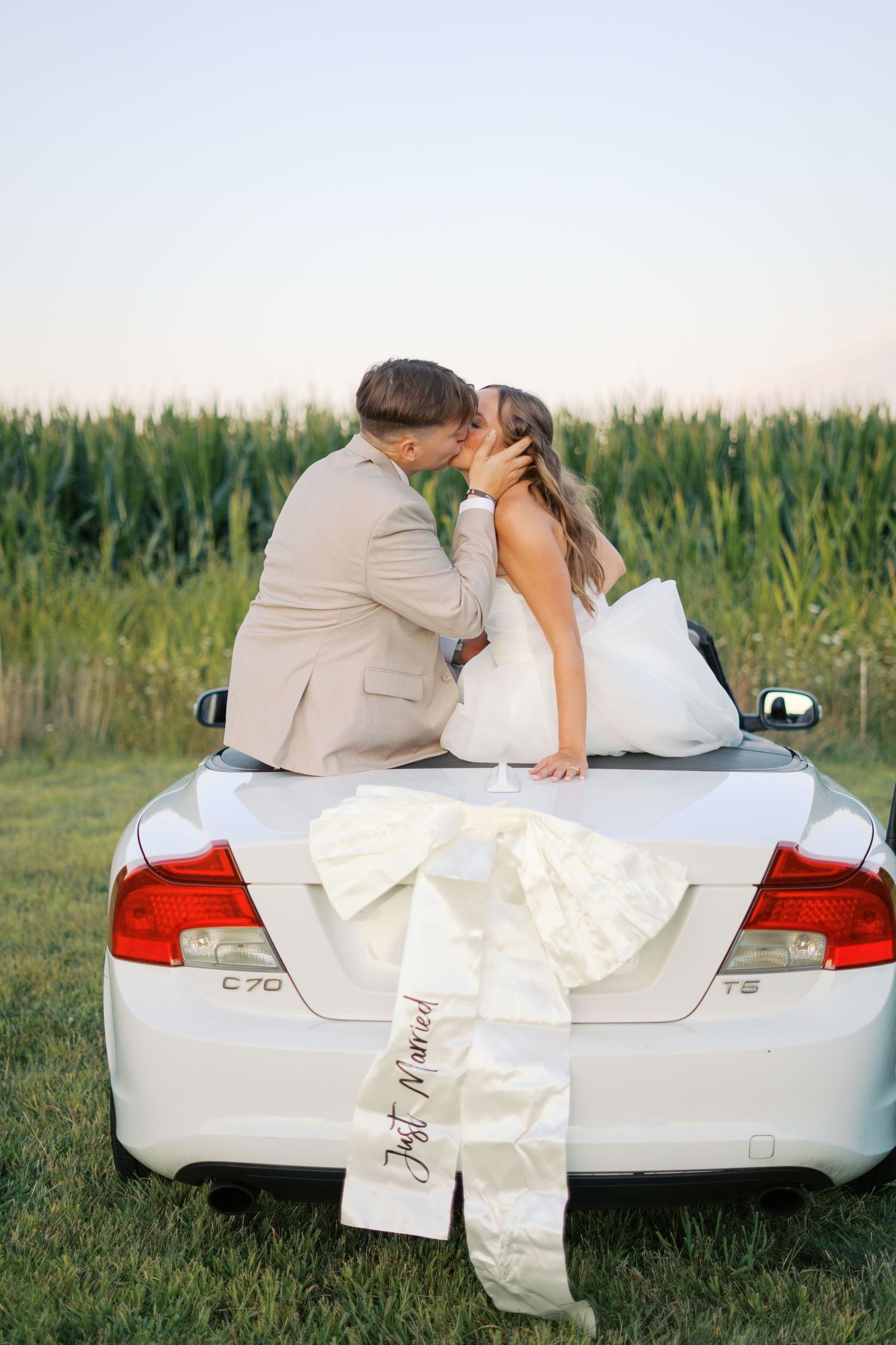 Intimate wedding photo shoot with couple on car trunk near cornfield.