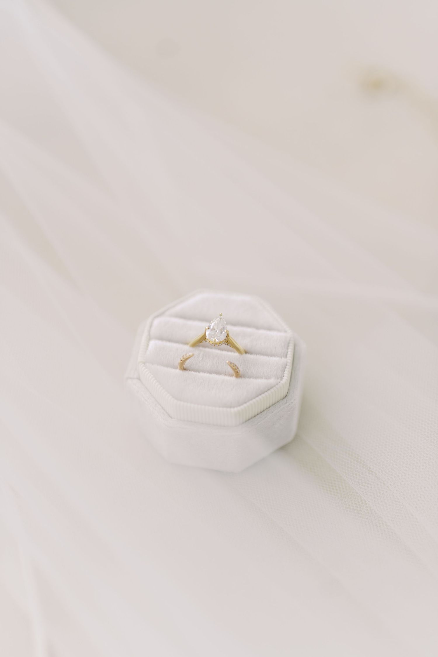 Wedding ring nestled in white fabric cushion against light background.