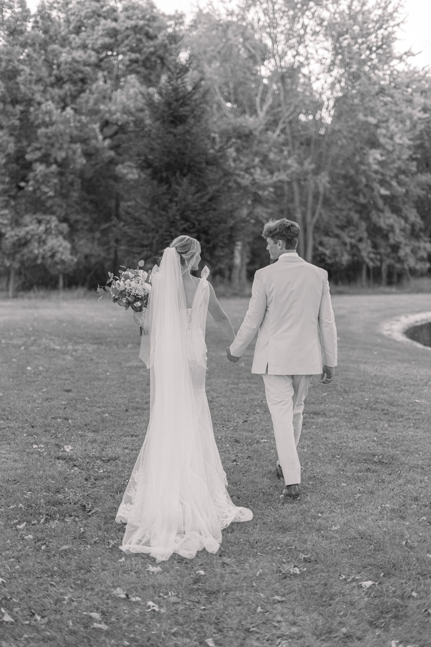 Black and white photo of couple walking hand in hand through garden path after ceremony.