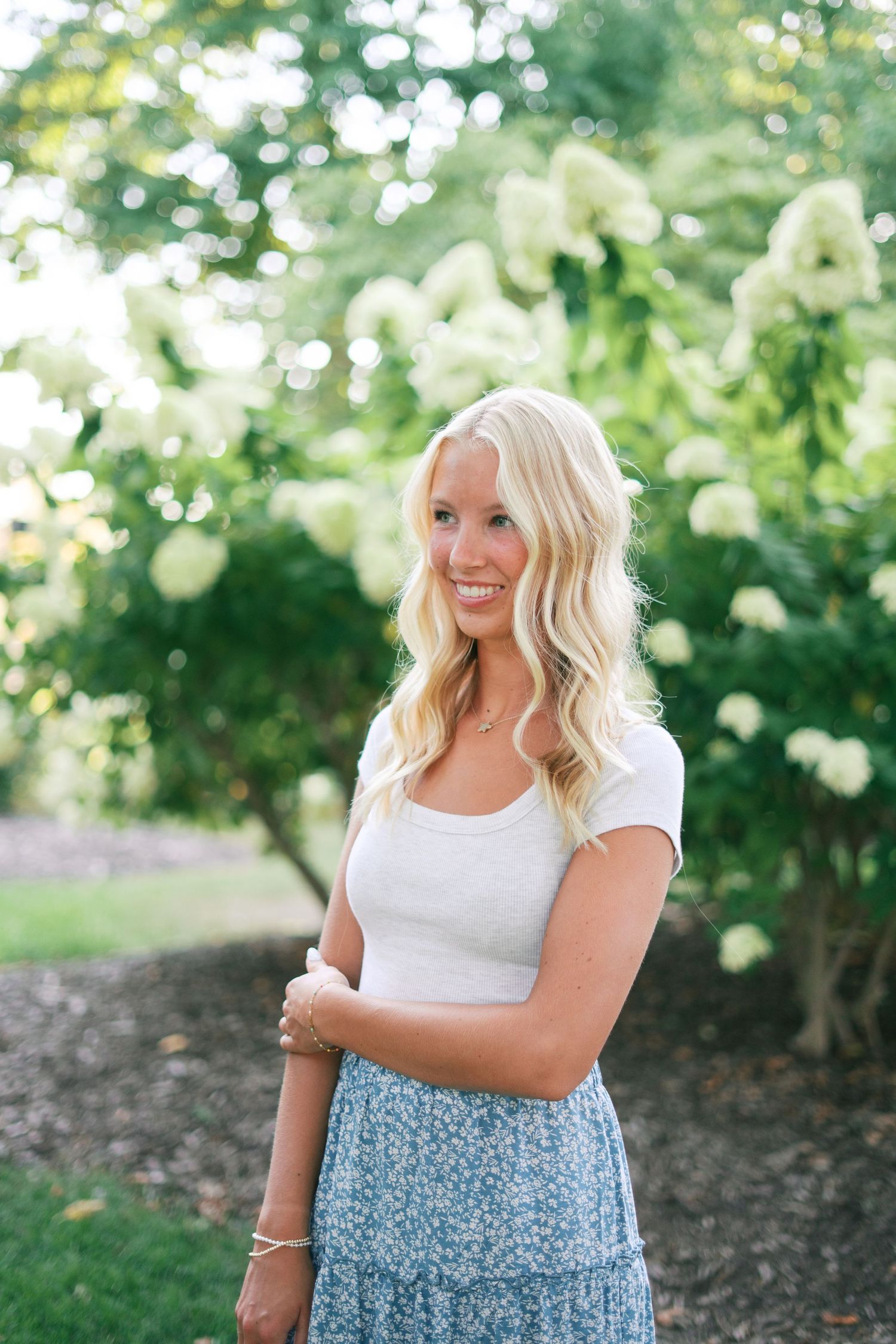 Summer portrait in white top and floral skirt with garden backdrop.