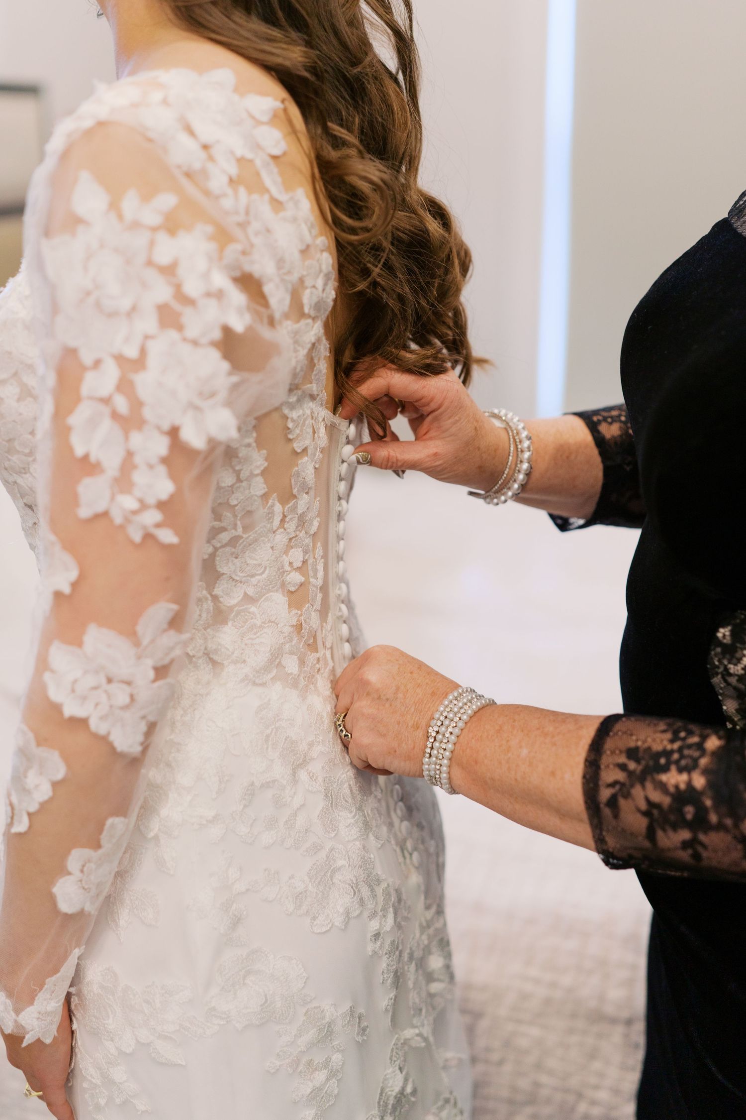 Close-up details of delicate lace and sheer elements on a wedding dress being fastened.