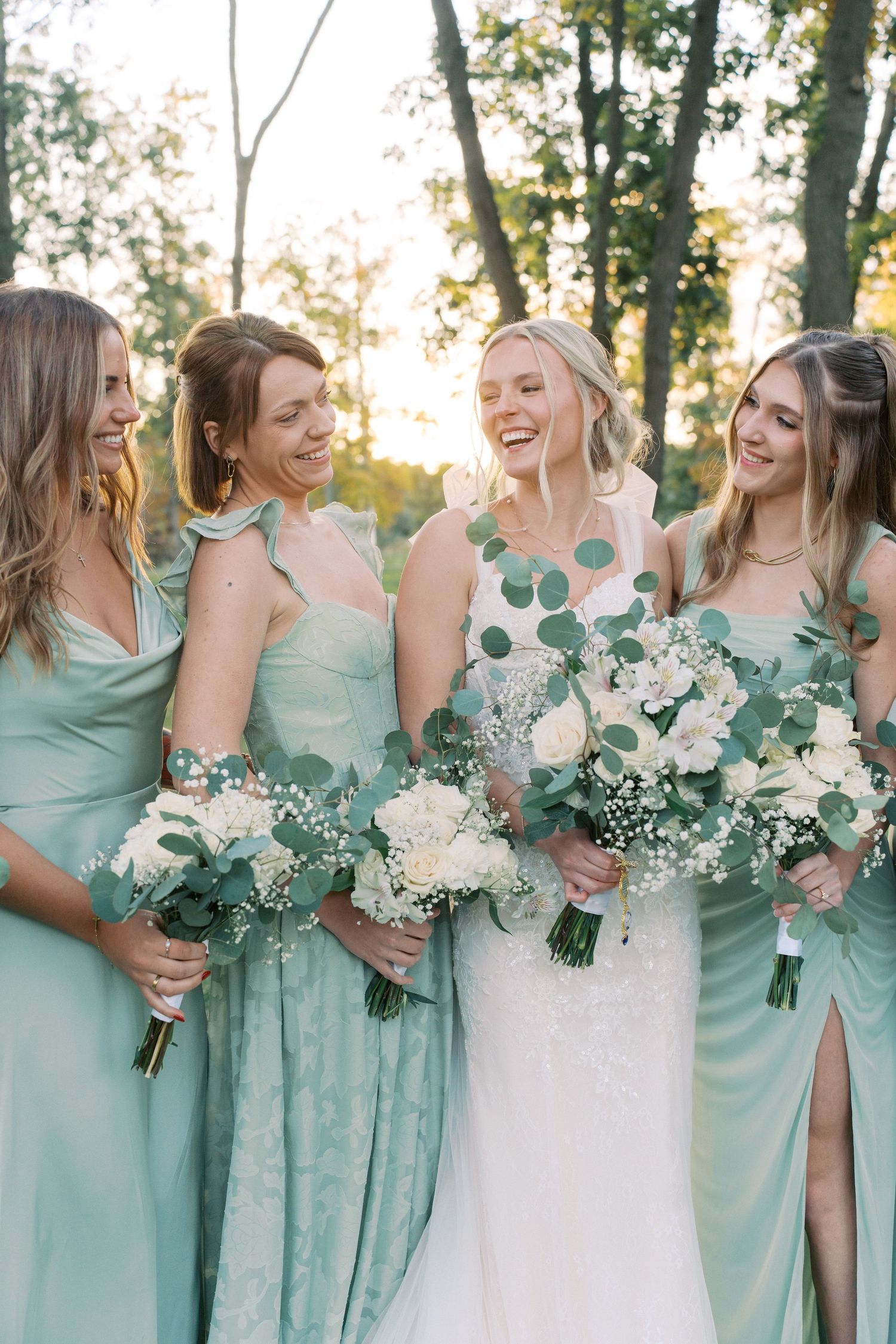Wedding party in mint green bridesmaid dresses posing with bouquets against a natural outdoor backdrop.