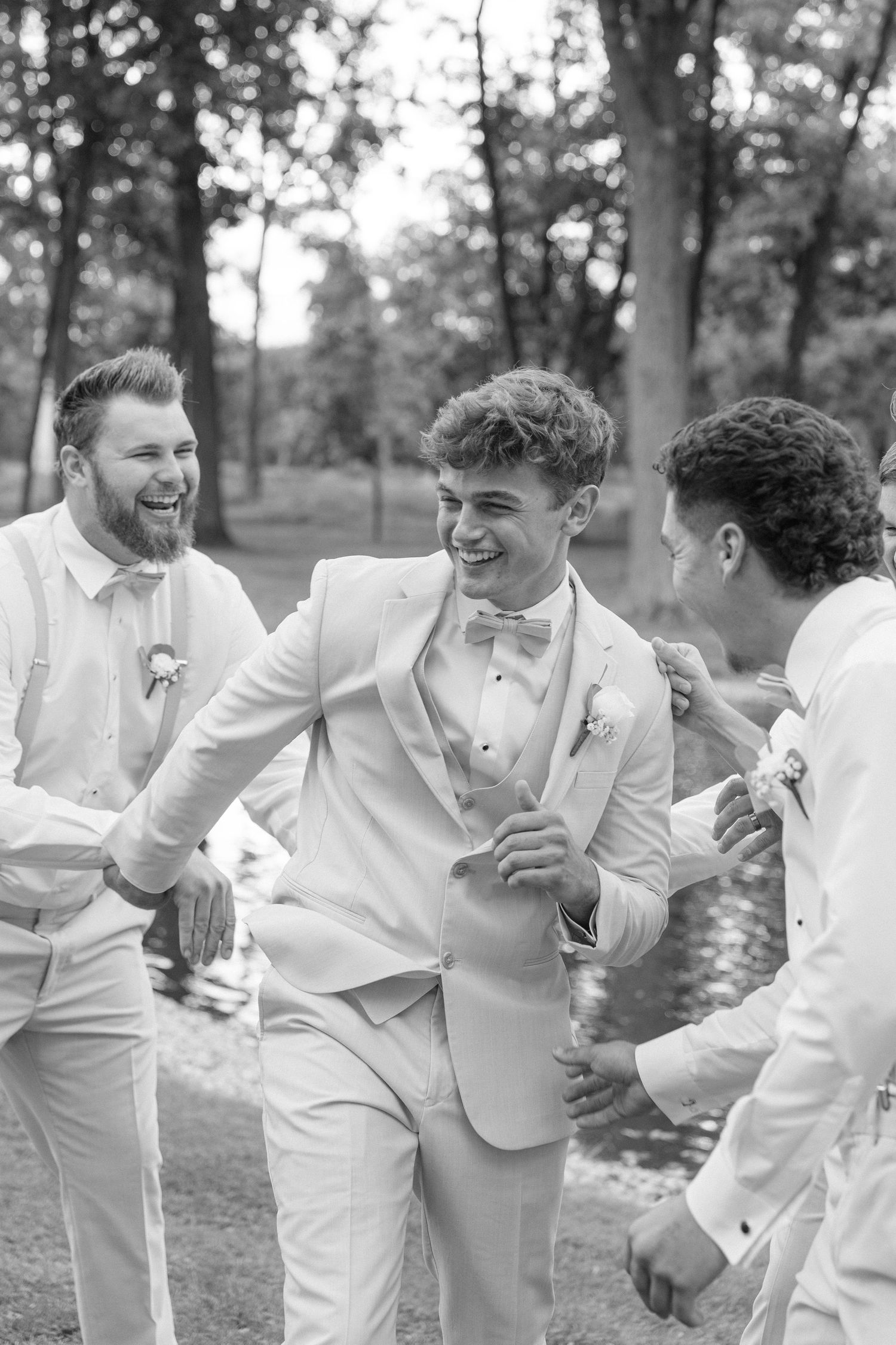 Groomsmen in white suits share a candid laughing moment during wedding photos.