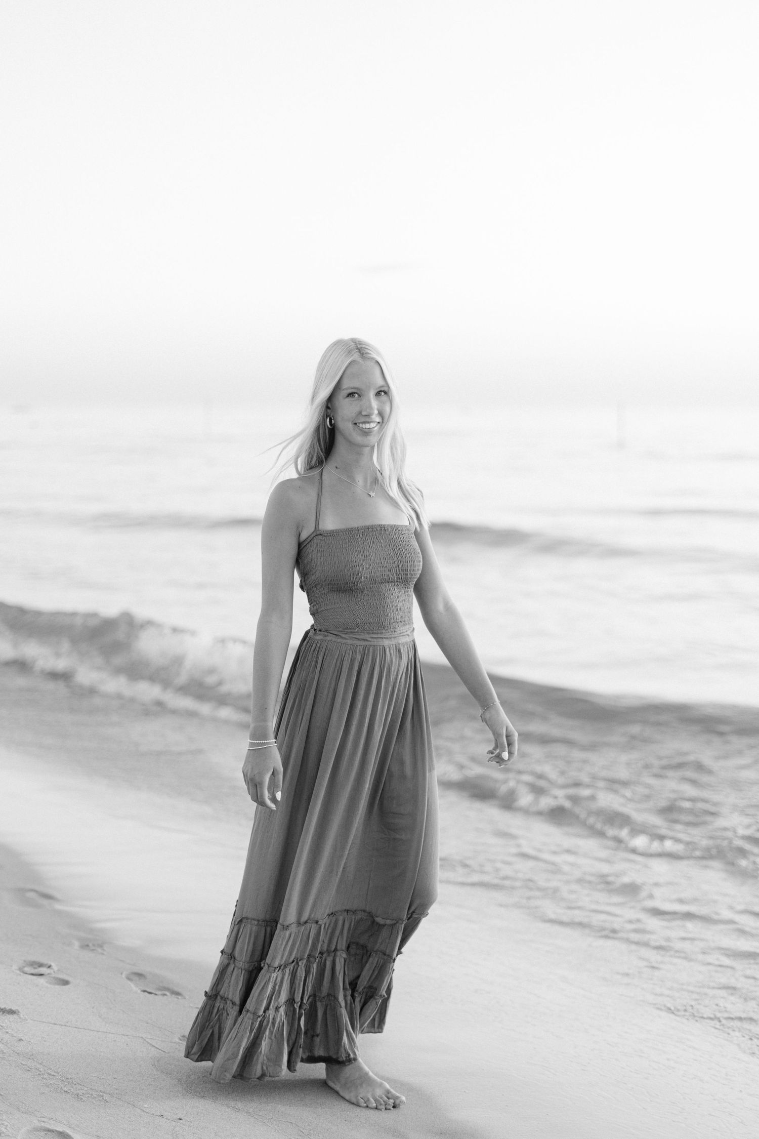 Person in a blue dress poses elegantly on a beach in black and white photography.