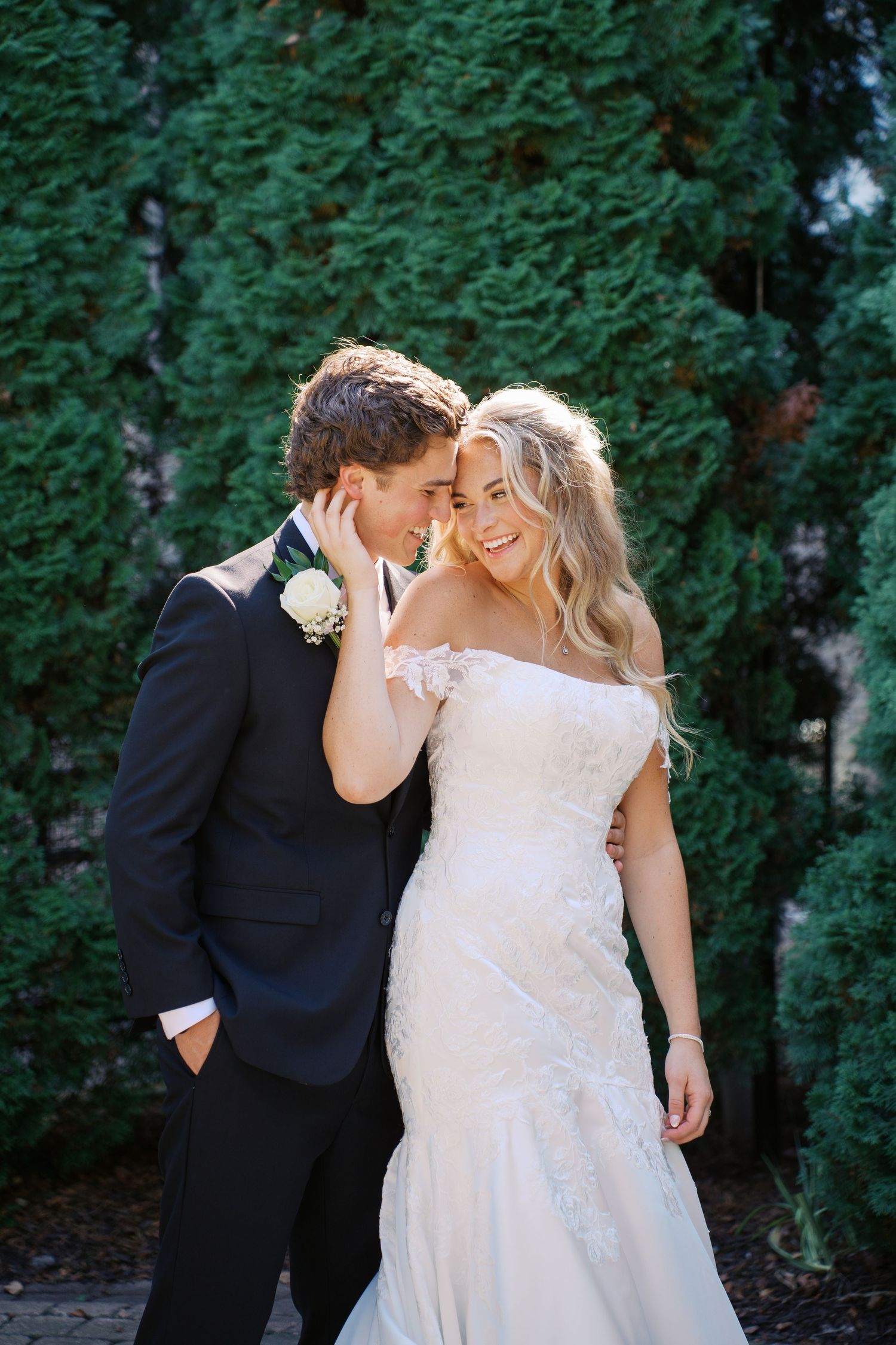 Romantic wedding couple poses against lush green garden backdrop.