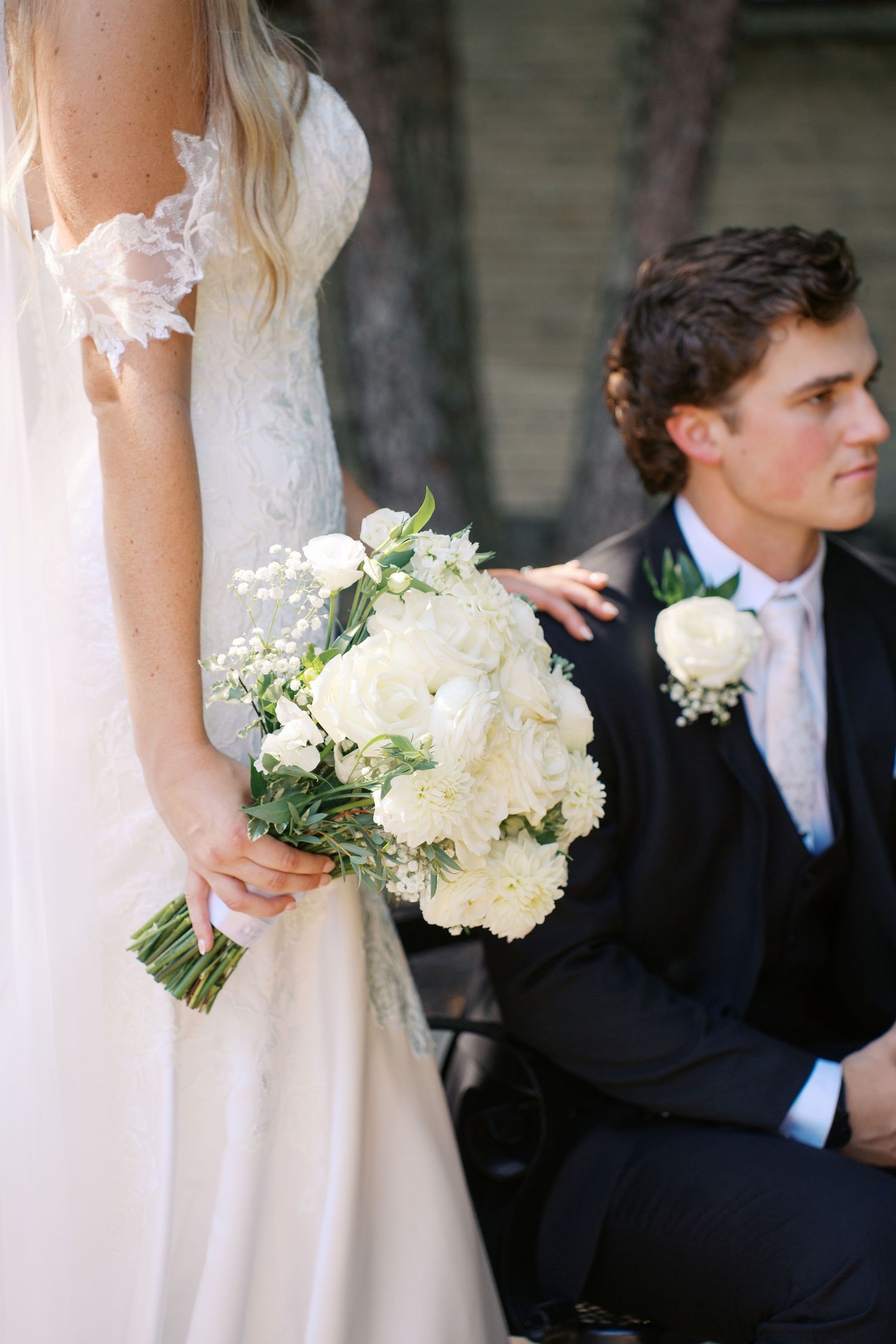 A white bridal bouquet with hydrangeas and baby's breath rests against a white dress.
