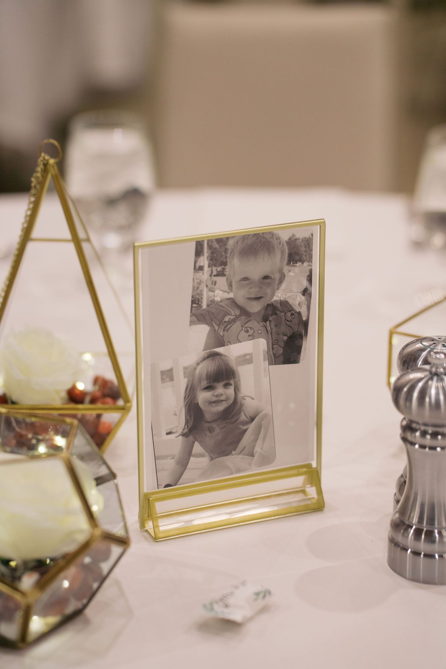 Gold-framed photo displays and decorative elements on white tablecloth at wedding reception.