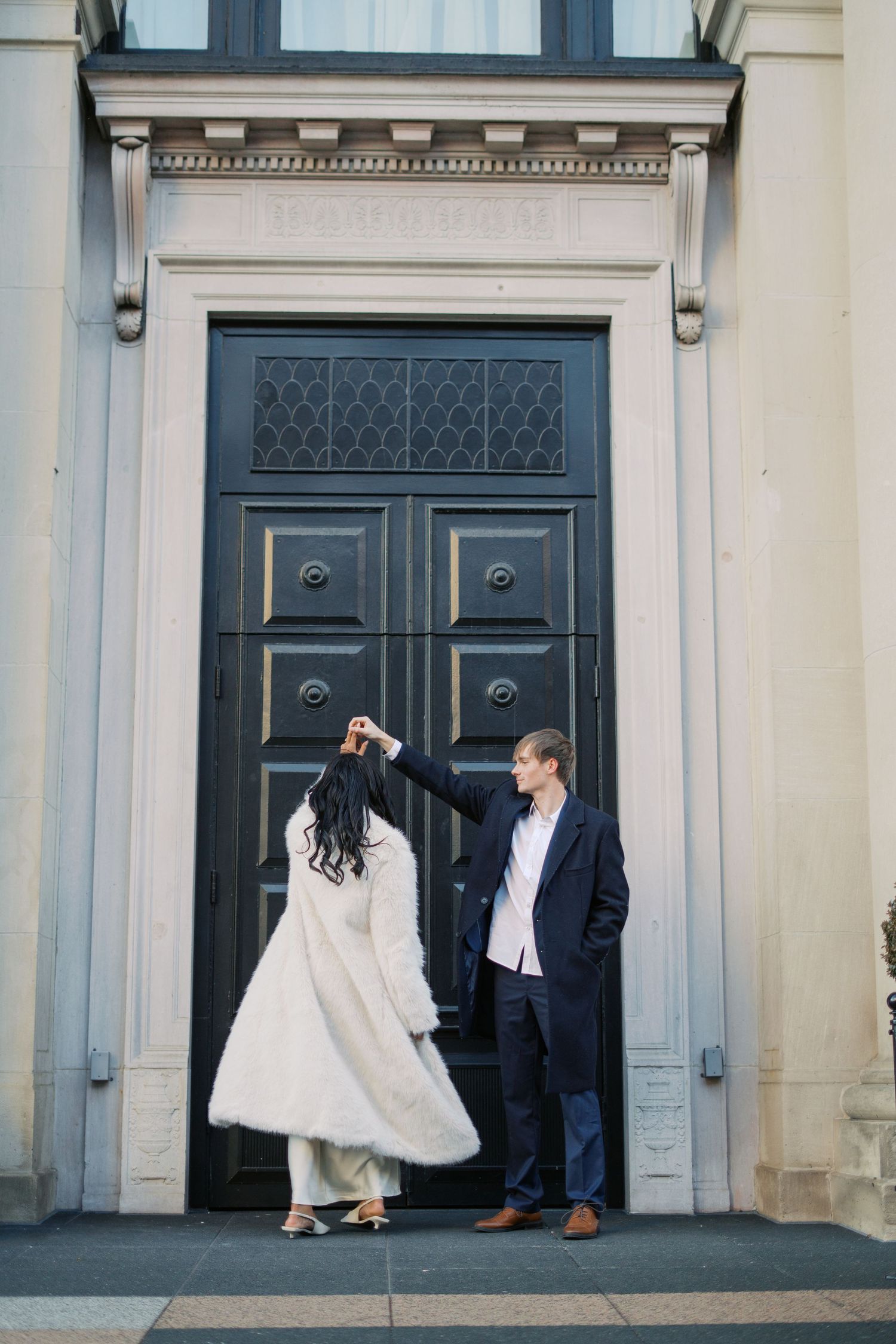 A couple poses against elegant black doors, with the bride wearing a white fur wrap and gown.